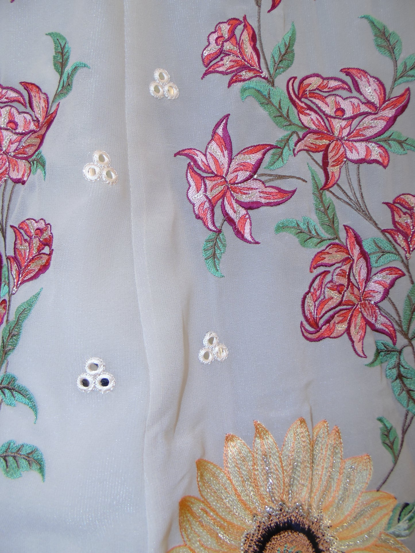 Close-up of floral embroidery with pink roses and green leaves on a white fabric background.