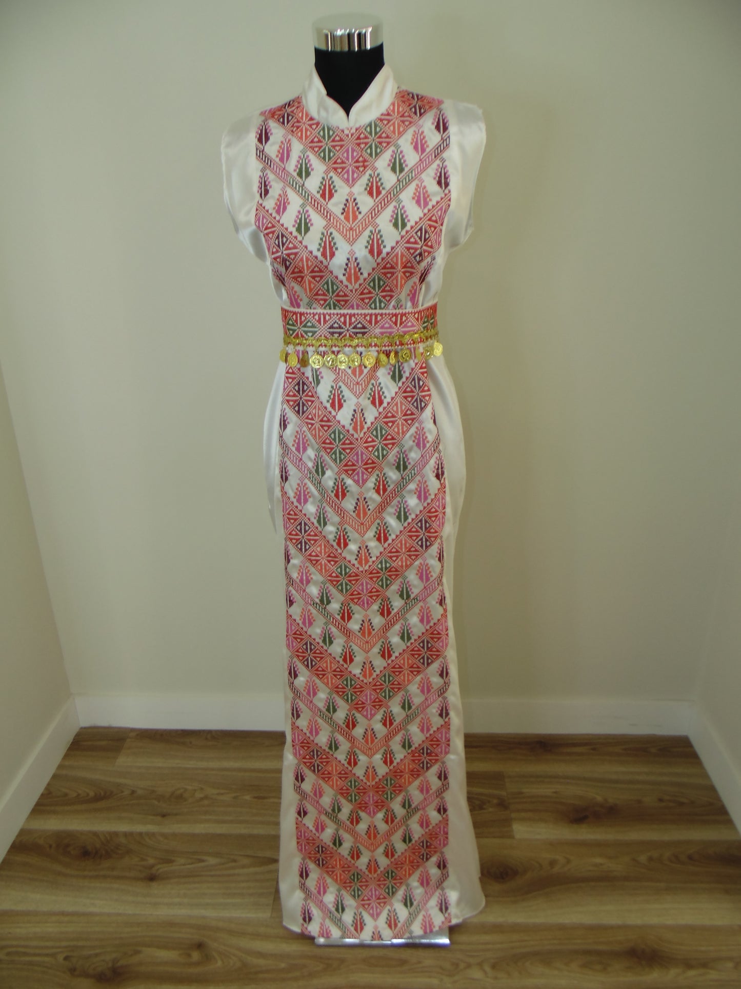 Traditional dress with intricate patterns on a mannequin against a plain wall.