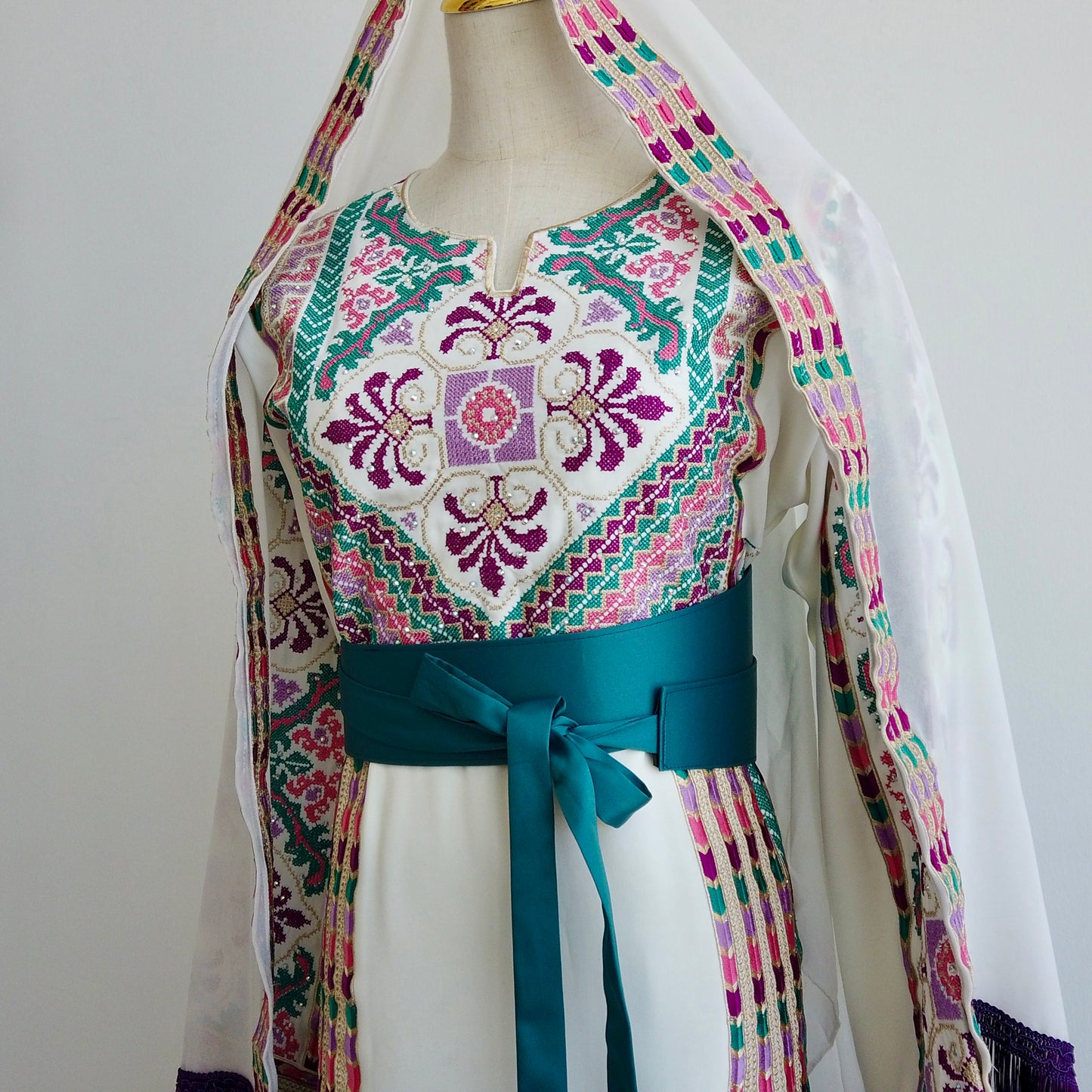 Front view of Palestinian thobe with purple, green, and pink embroidery and teal belt - displayed on a mannequin