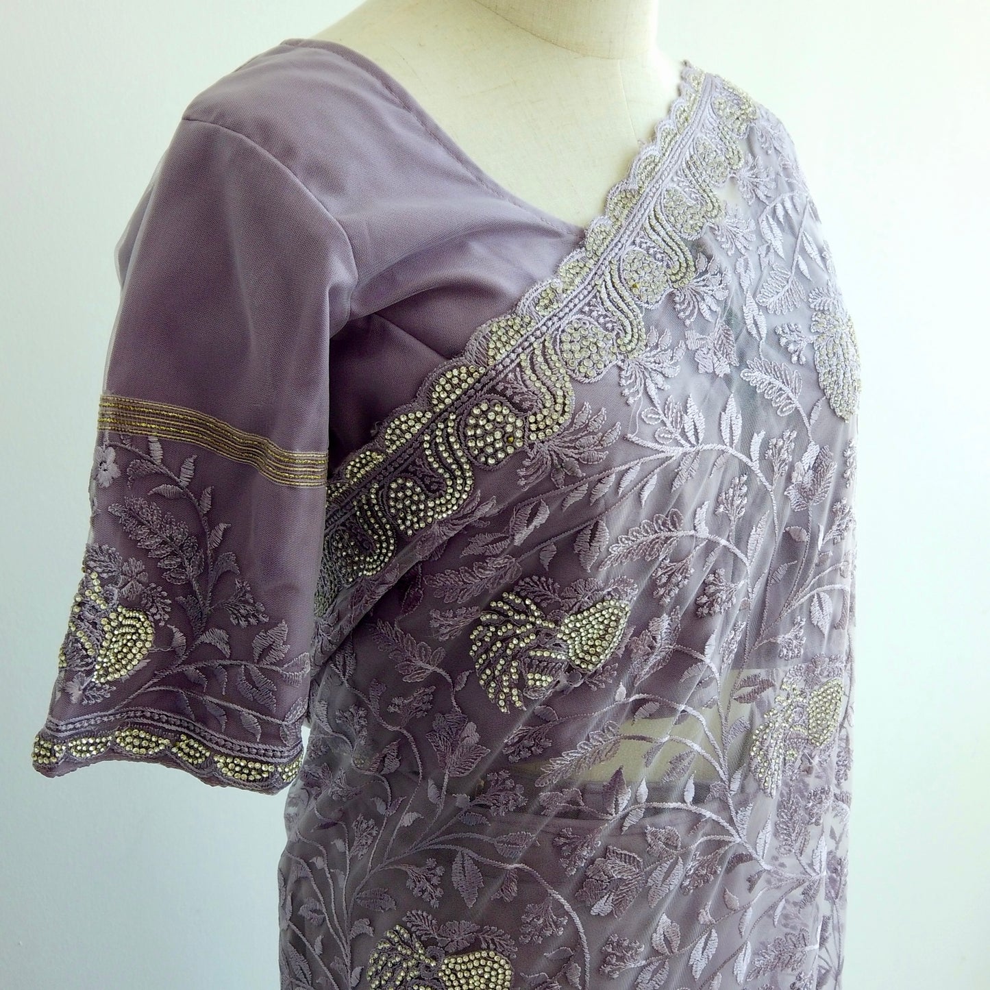 Embroidered purple blouse with floral patterns on a mannequin against a white background