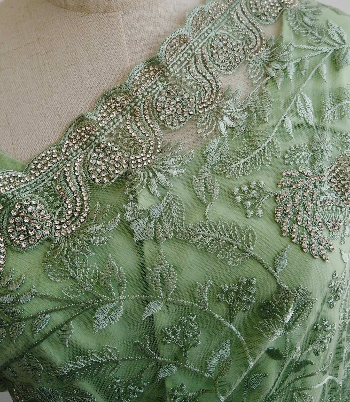Close-up of green embroidered fabric with intricate patterns on a mannequin.
