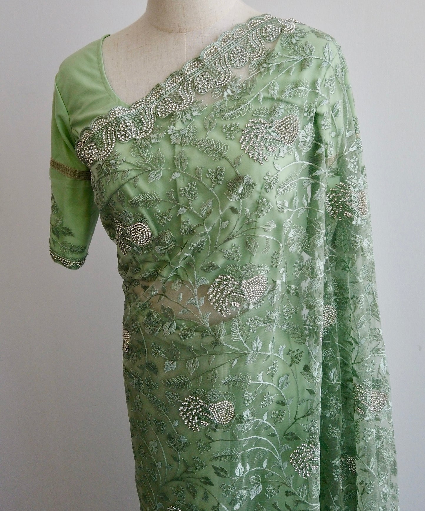 Green net ready-to-wear saree with silver floral embroidery displayed on a mannequin.