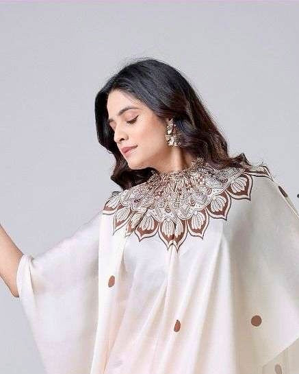 Woman wearing a cream saree with intricate designs, branded 'Arisca'.