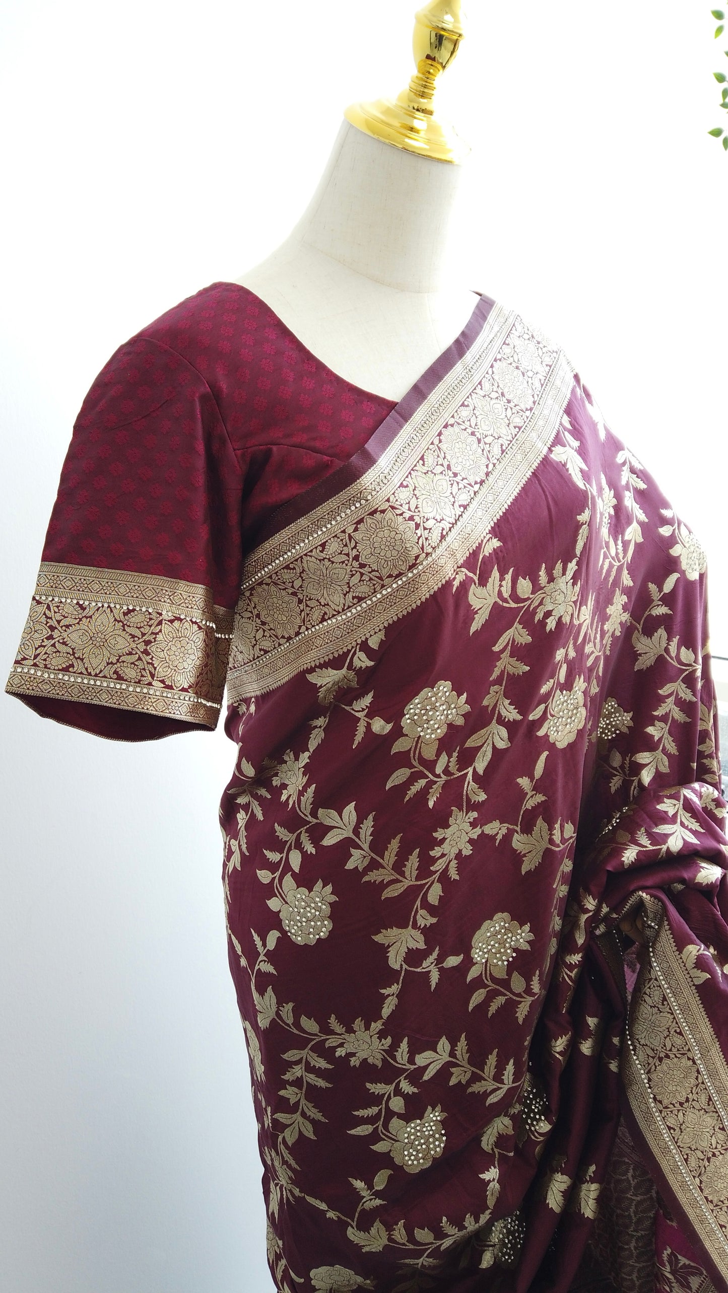 Maroon saree with gold embroidery on a mannequin against a white background