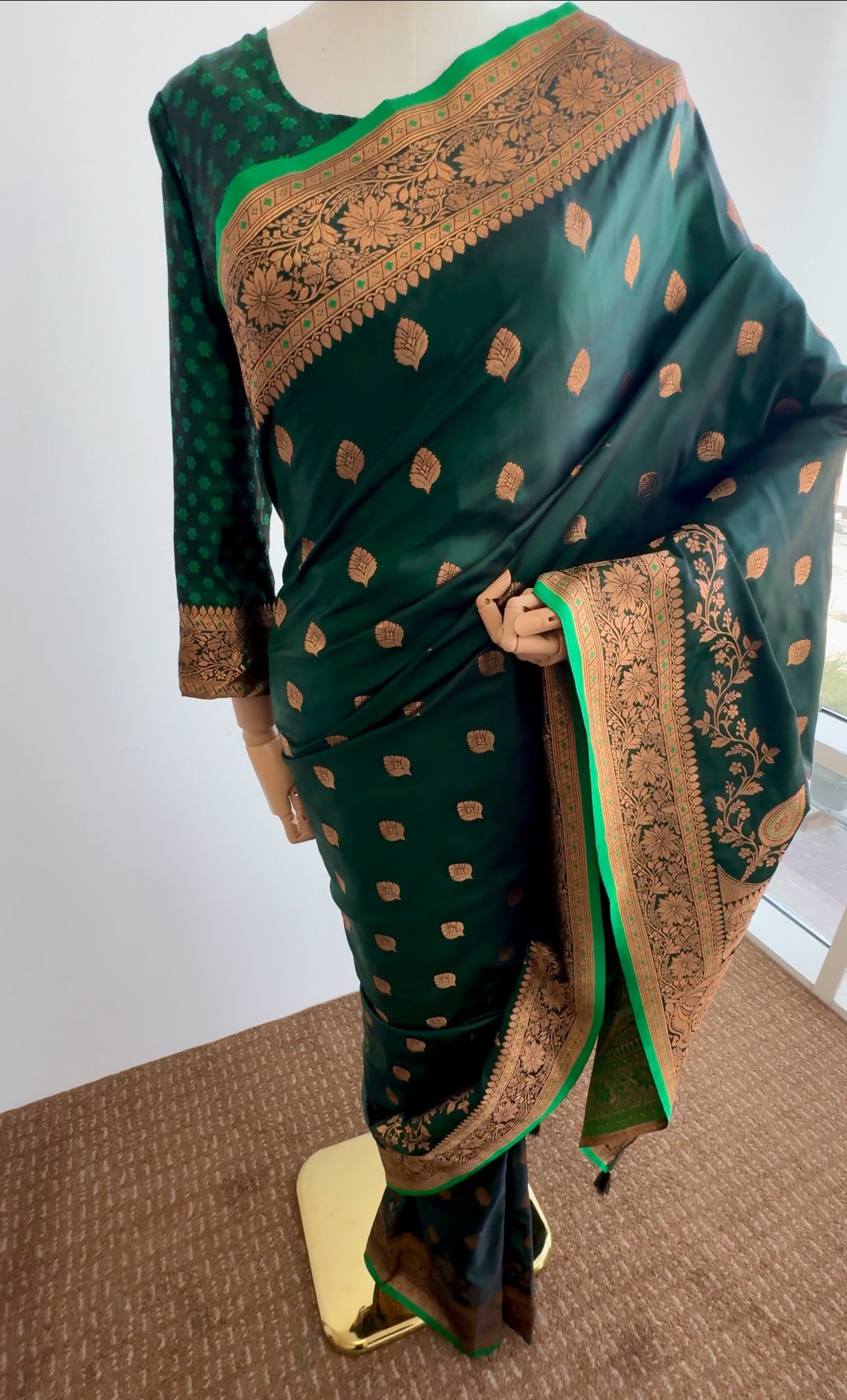 Green satin silk saree with gold patterns on a mannequin against a white background