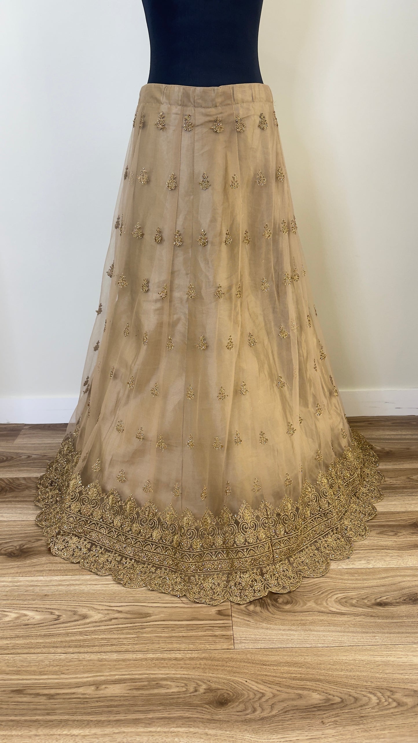 Golden embroidered skirt on a wooden floor with a white wall background
