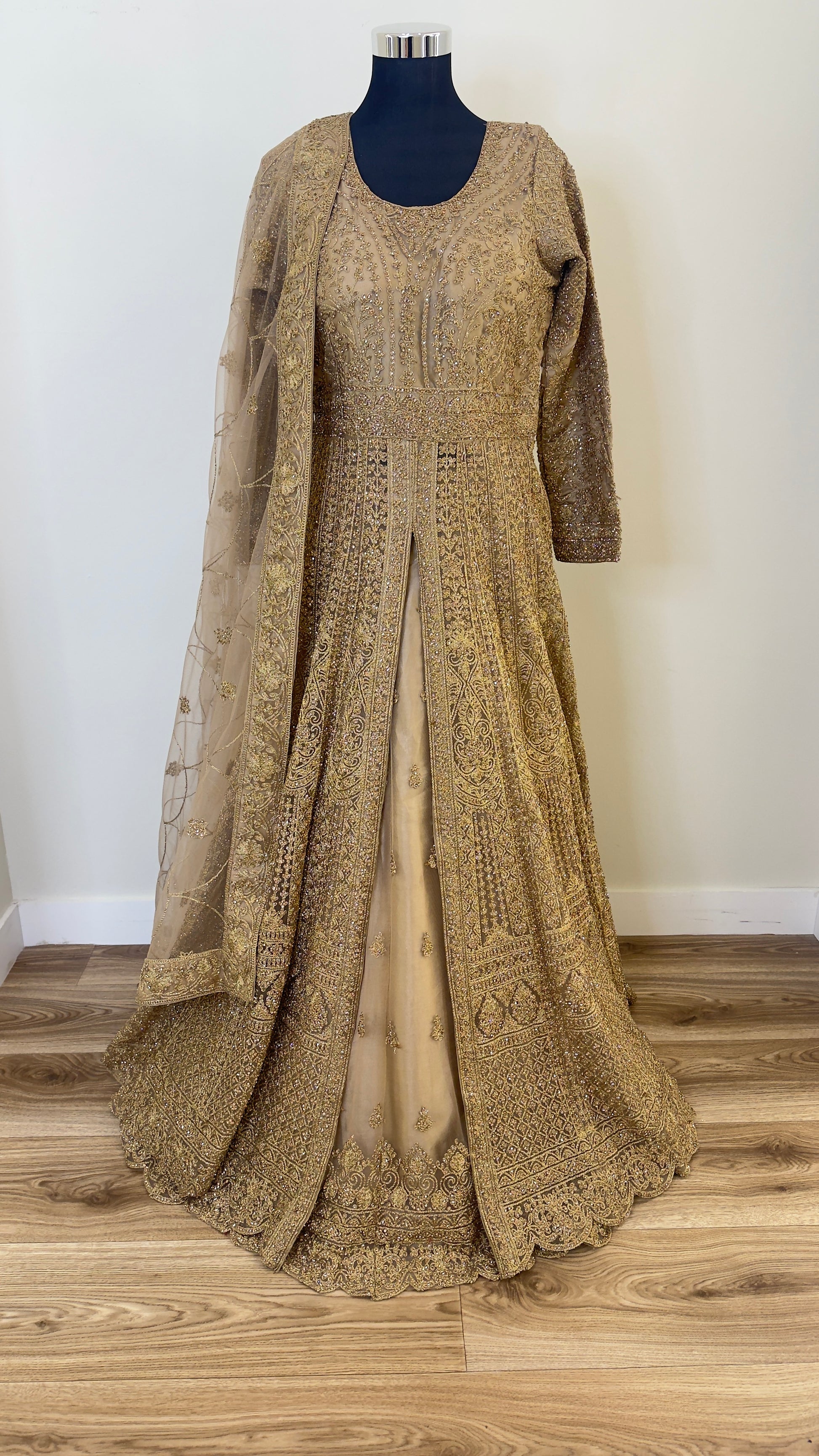 Golden embroidered traditional outfit on a mannequin against a white wall.