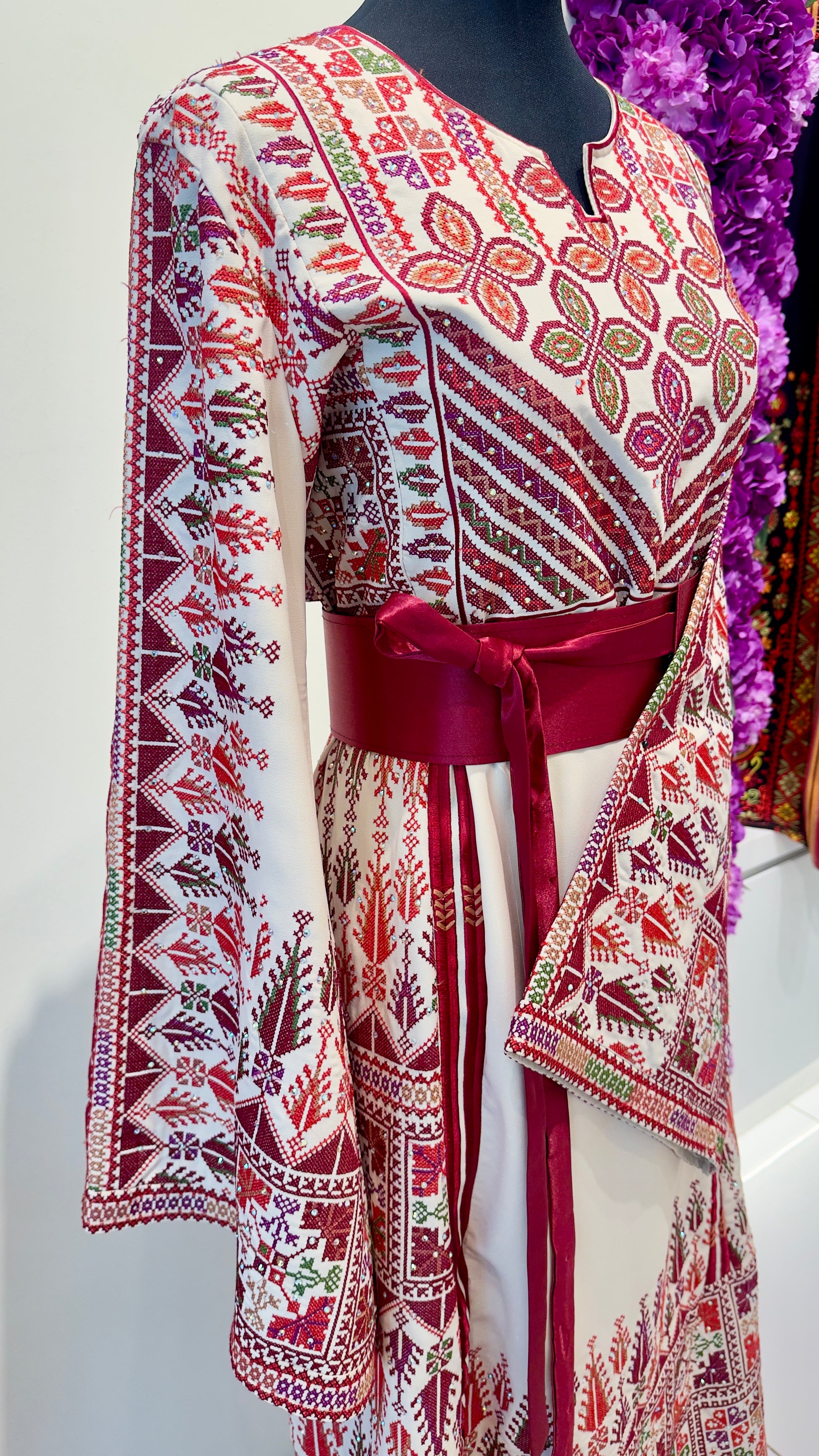 Traditional outfit with a patterned Palestinian Thobe on a mannequin against a purple floral background.