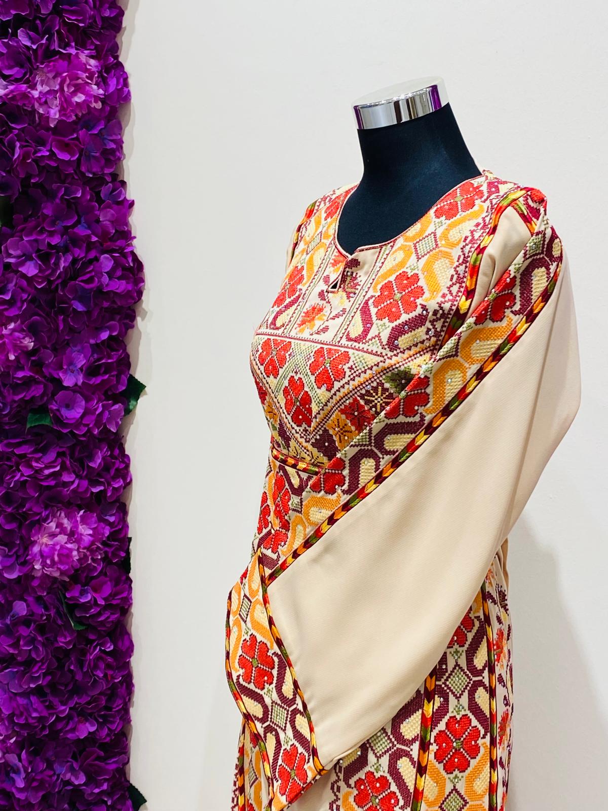 Champagne beige Palestinian-inspired thobe with red and orange geometric embroidery at Arisca Qatar.