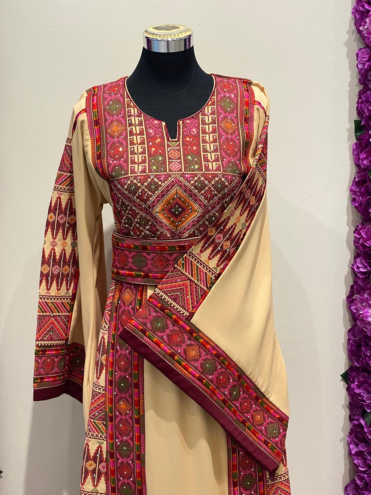 Beige Palestinian-inspired thobe with burgundy and olive green geometric embroidery at Arisca Qatar.