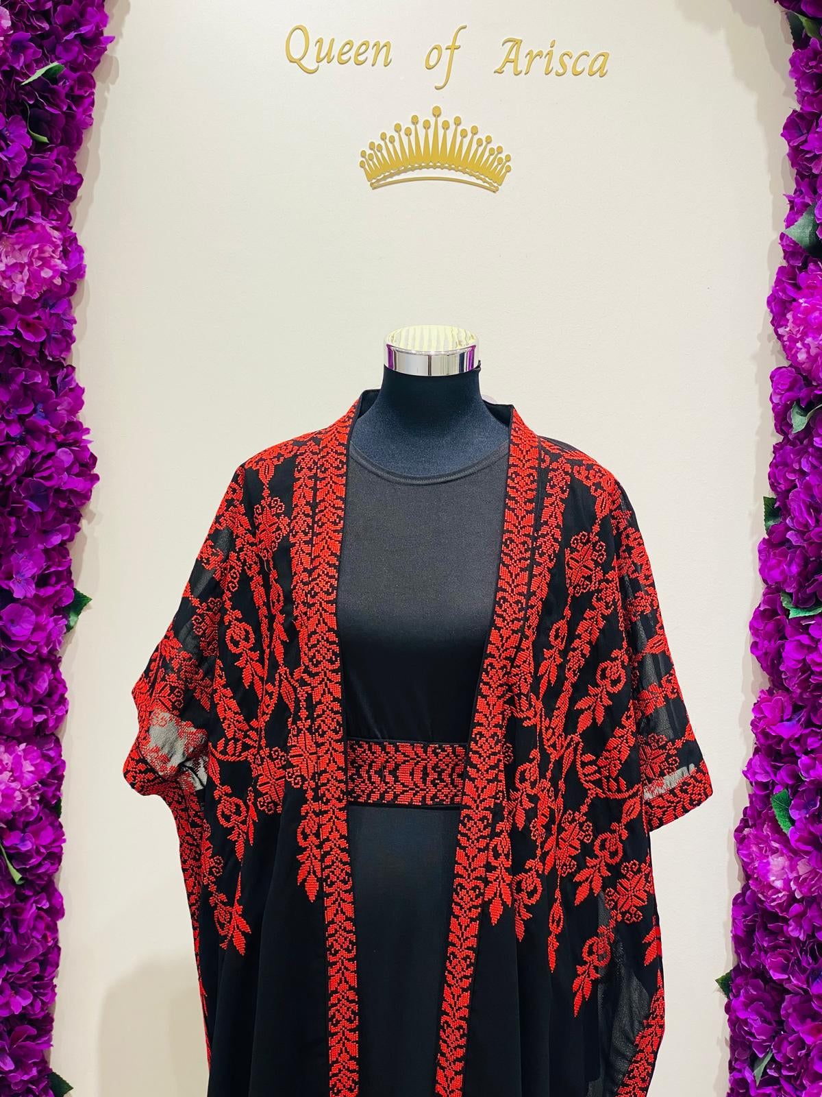 A black and red embroidered open-front cardigan draped over a black dress.