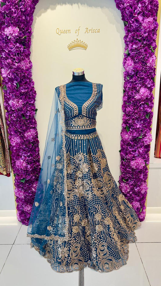 Blue embroidered lehenga with gold details on a mannequin against a decorative background.
