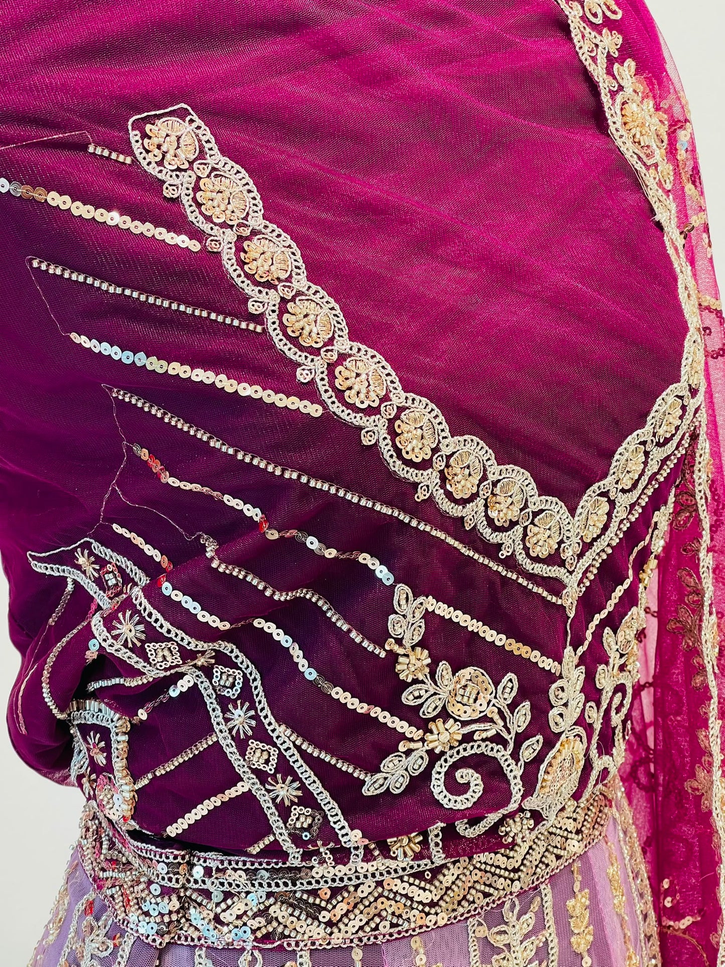 A close-up of a rich magenta-purple velvet fabric of lehenga, decorated with intricate gold and silver zari embroidery, sequins, and mirror work