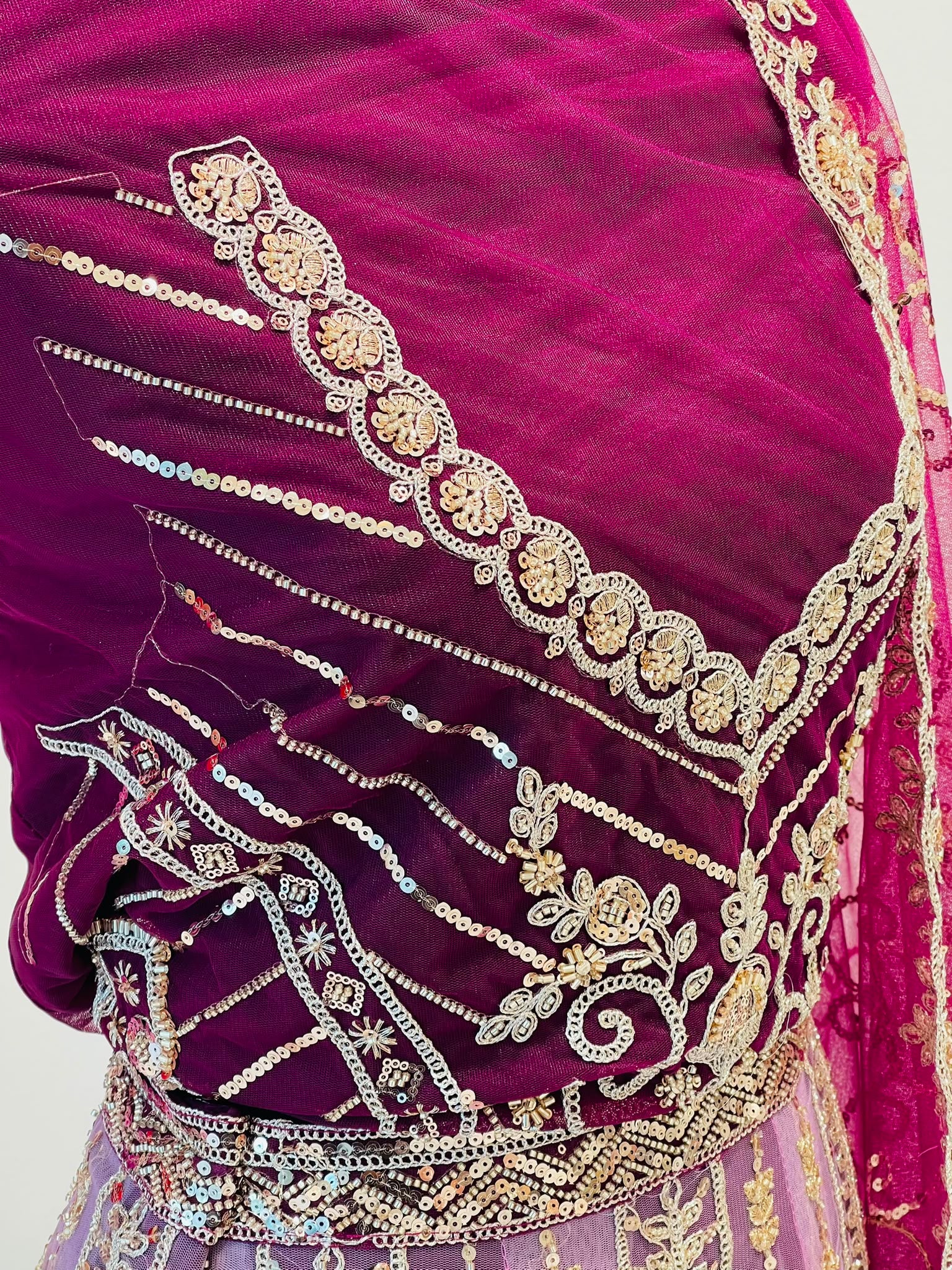 A close-up of a rich magenta-purple velvet fabric of lehenga, decorated with intricate gold and silver zari embroidery, sequins, and mirror work