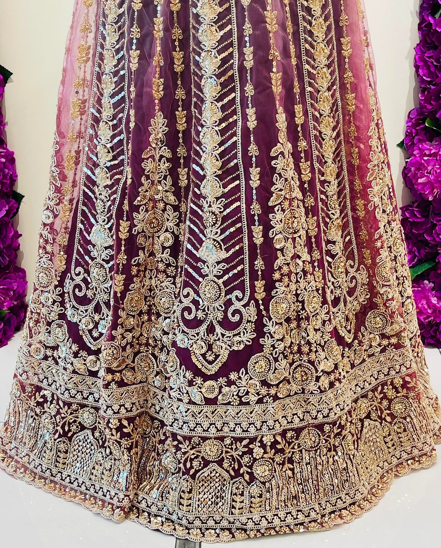 A close-up of an ornate traditional skirt of lehenga in deep purple with extensive gold embroidery and metallic embellishments.