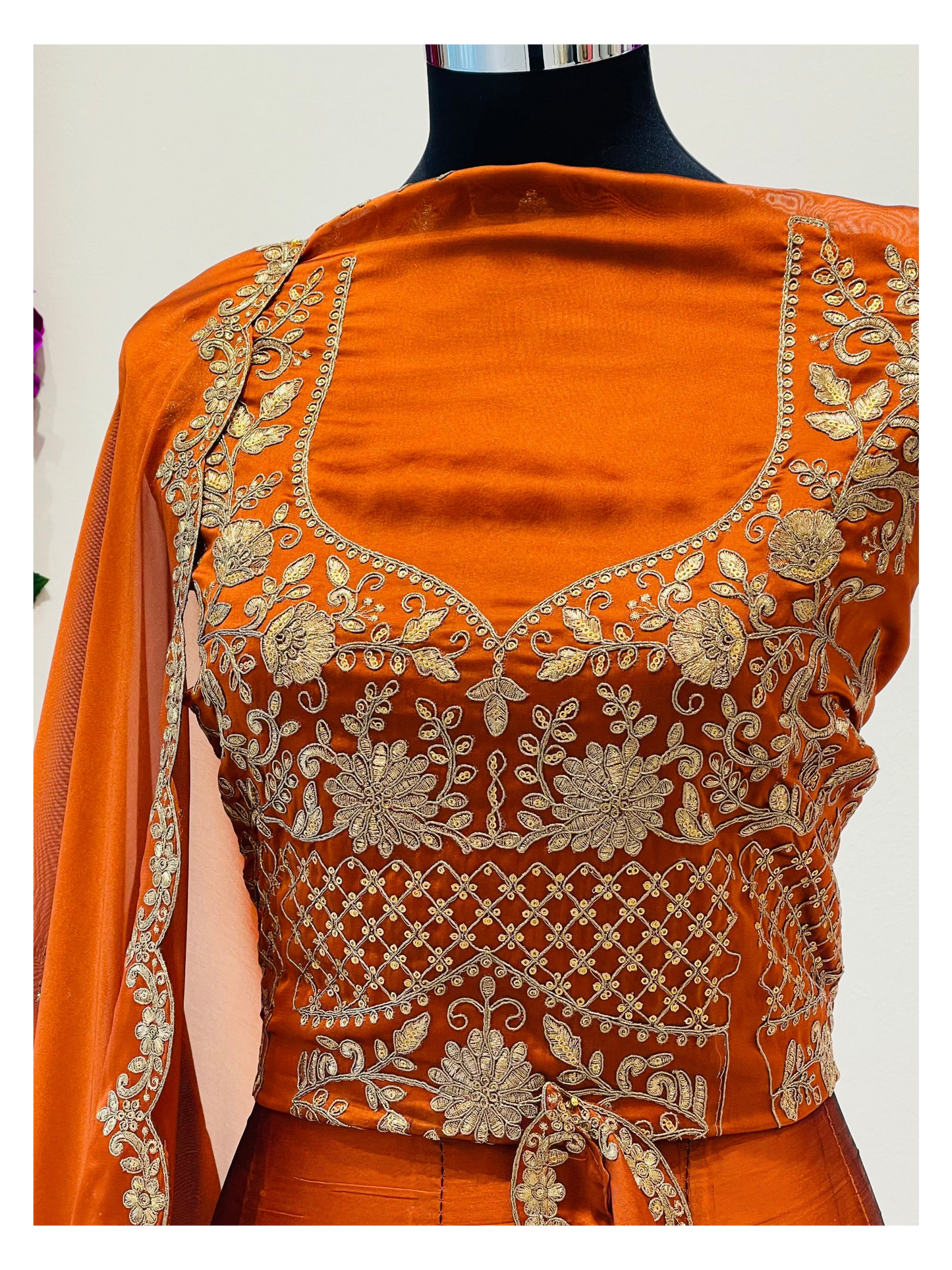 An orange embroidered traditional blouse  , featuring intricate gold floral and geometric embroidery, paired with a matching orange dupatta draped over one shoulder.