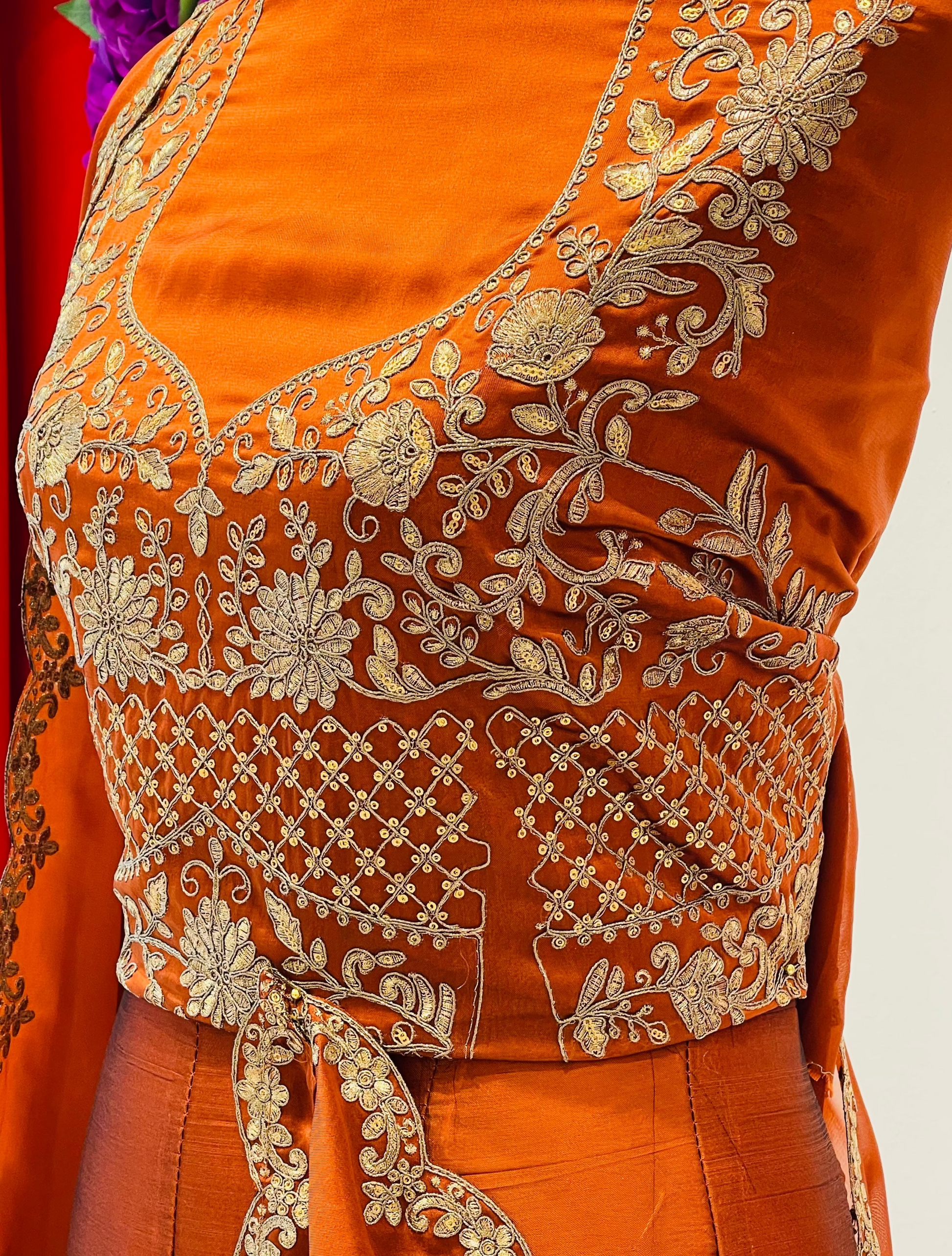 Close-up of an orange traditional garment with extensive gold floral embroidery on the bodice and waist tie.