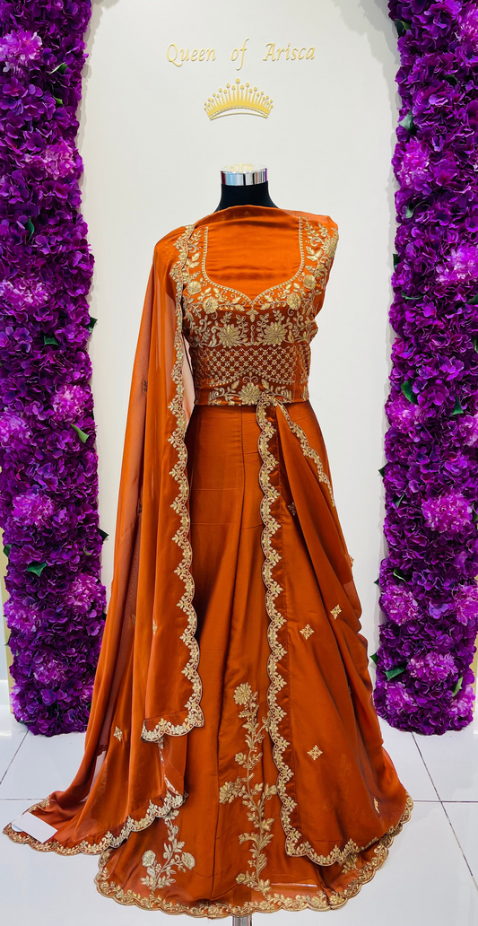 An orange traditional Indian lehenga with gold embroidery. The dress features a heavily embellished gold bodice, a matching orange skirt with gold border detailing, and a draped dupatta.