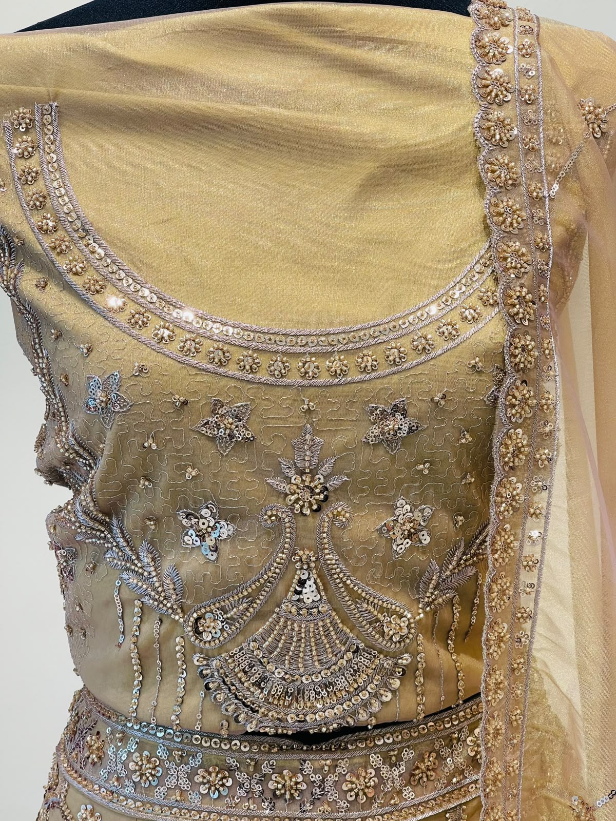 Close-up of a beige embellished traditional lehenga with intricate silver and gold embroidery, beadwork, and a matching sheer dupatta draped over the shoulder.