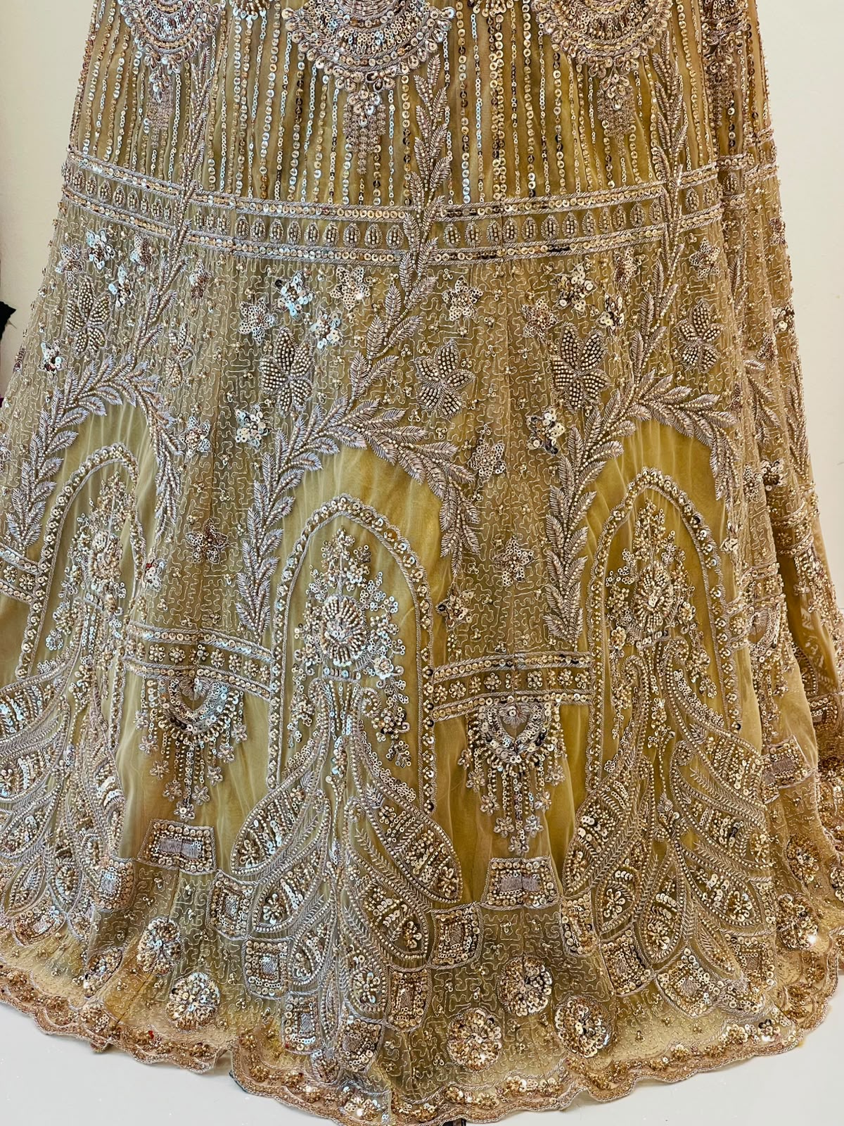 Close-up of an ornate gold and silver embellished skirt of lehenga with intricate beadwork, sequins, and embroidery on a sheer mesh fabric.