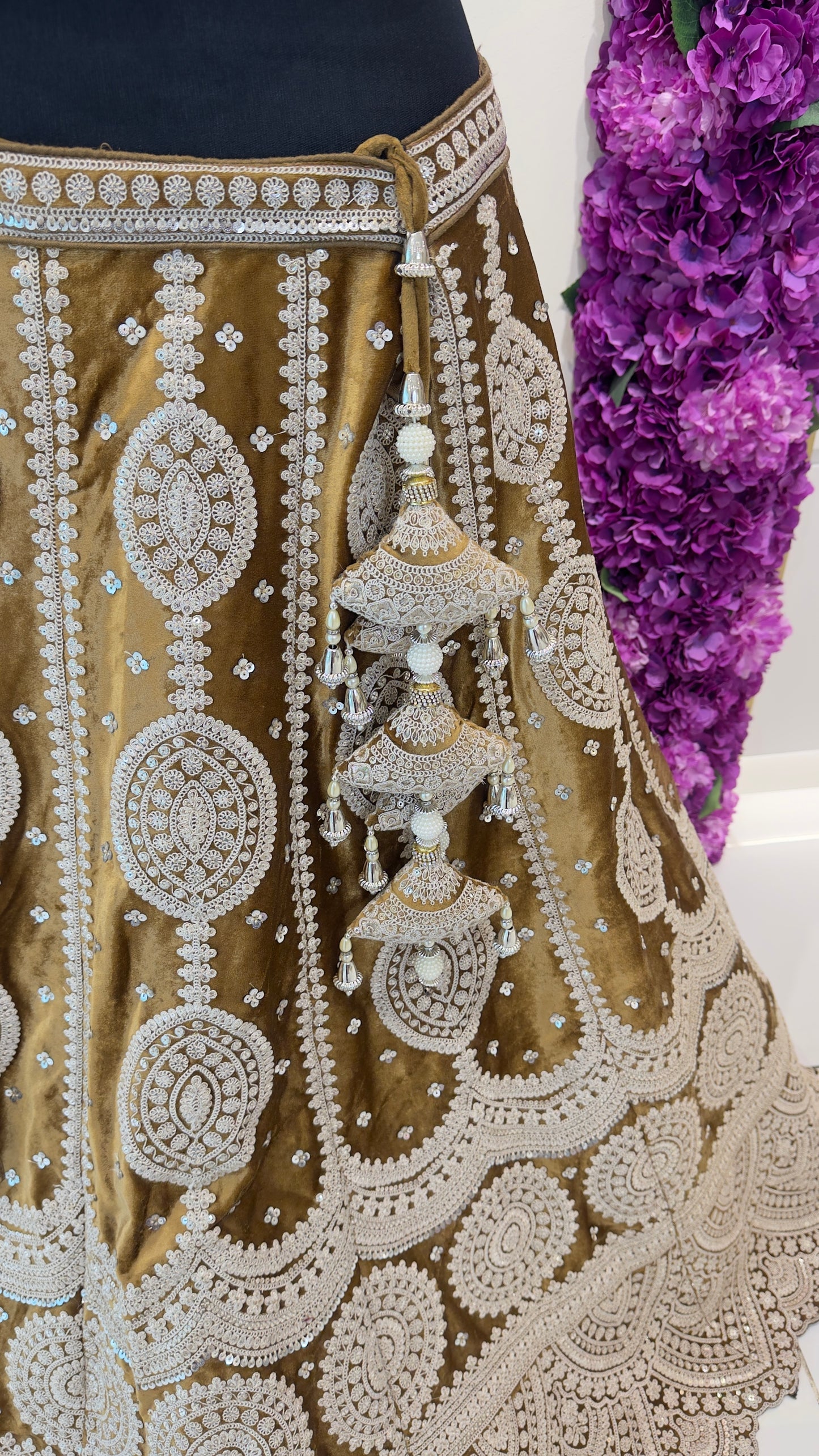 Decorative gold skirt with intricate white embroidery and purple flowers in the background
