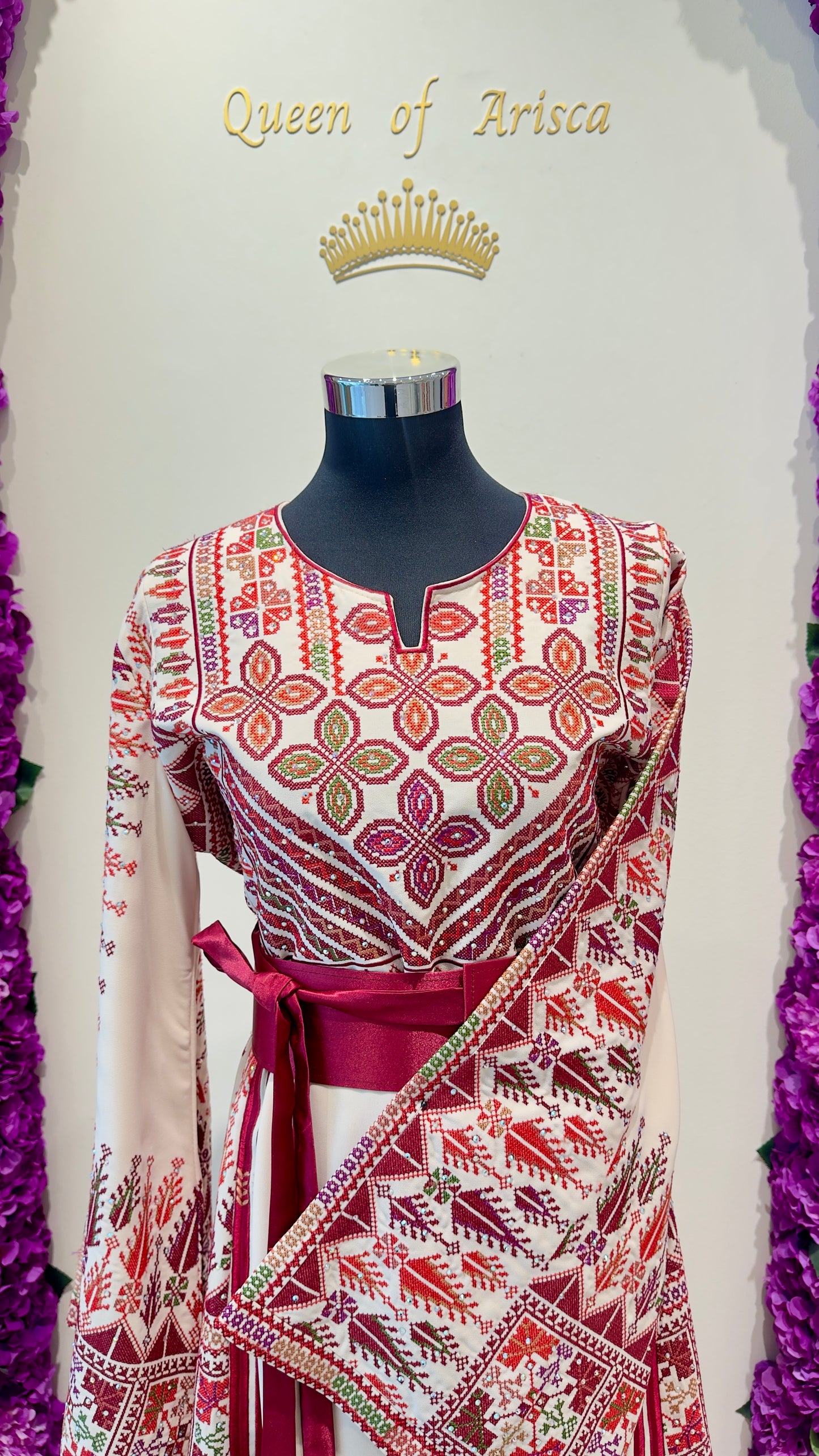 Mannequin wearing a red and white patterned dress with 'Queen of Arisca' text and crown above.