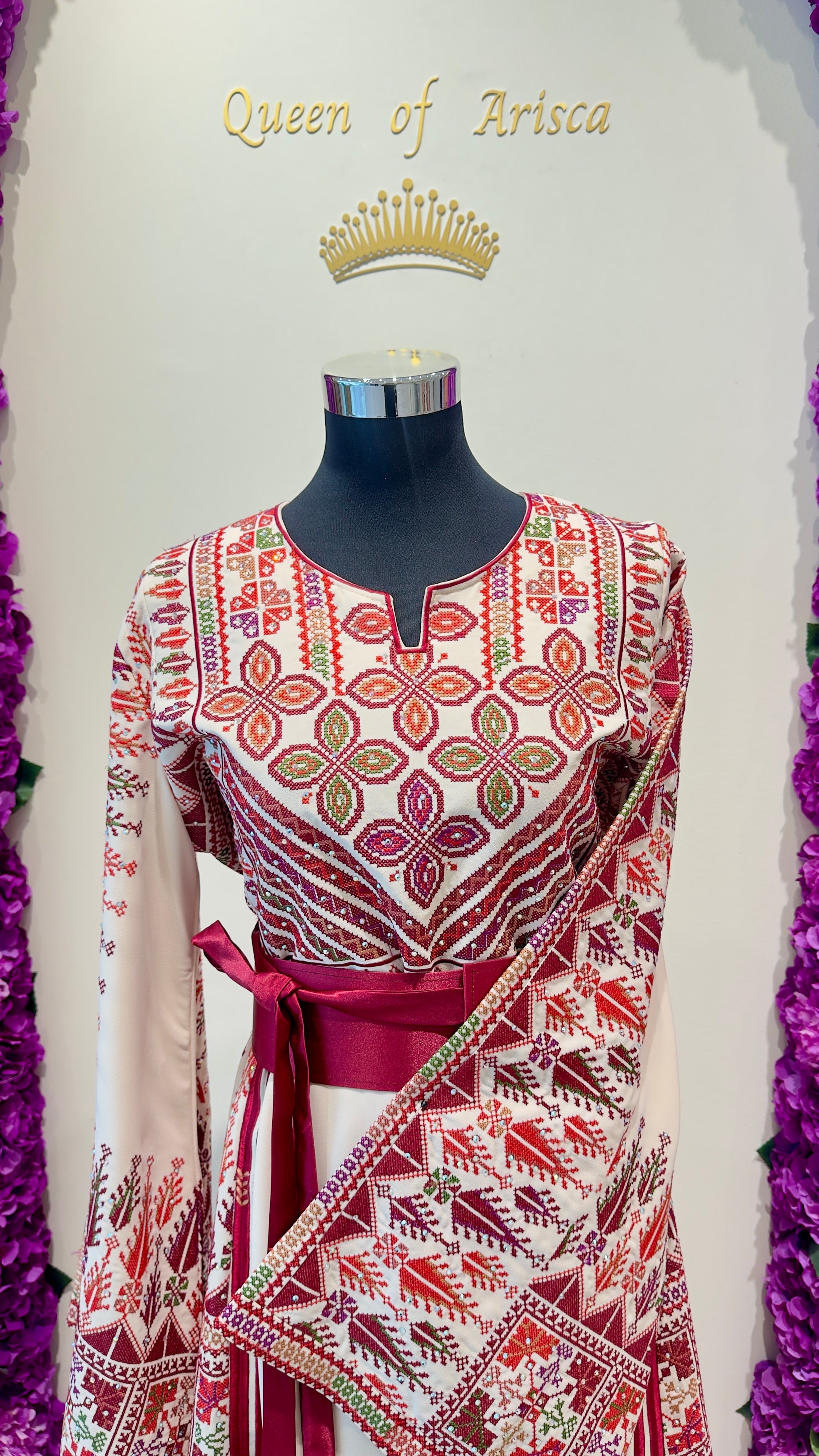 Mannequin wearing a red and white patterned dress with 'Queen of Arisca' text and crown above.