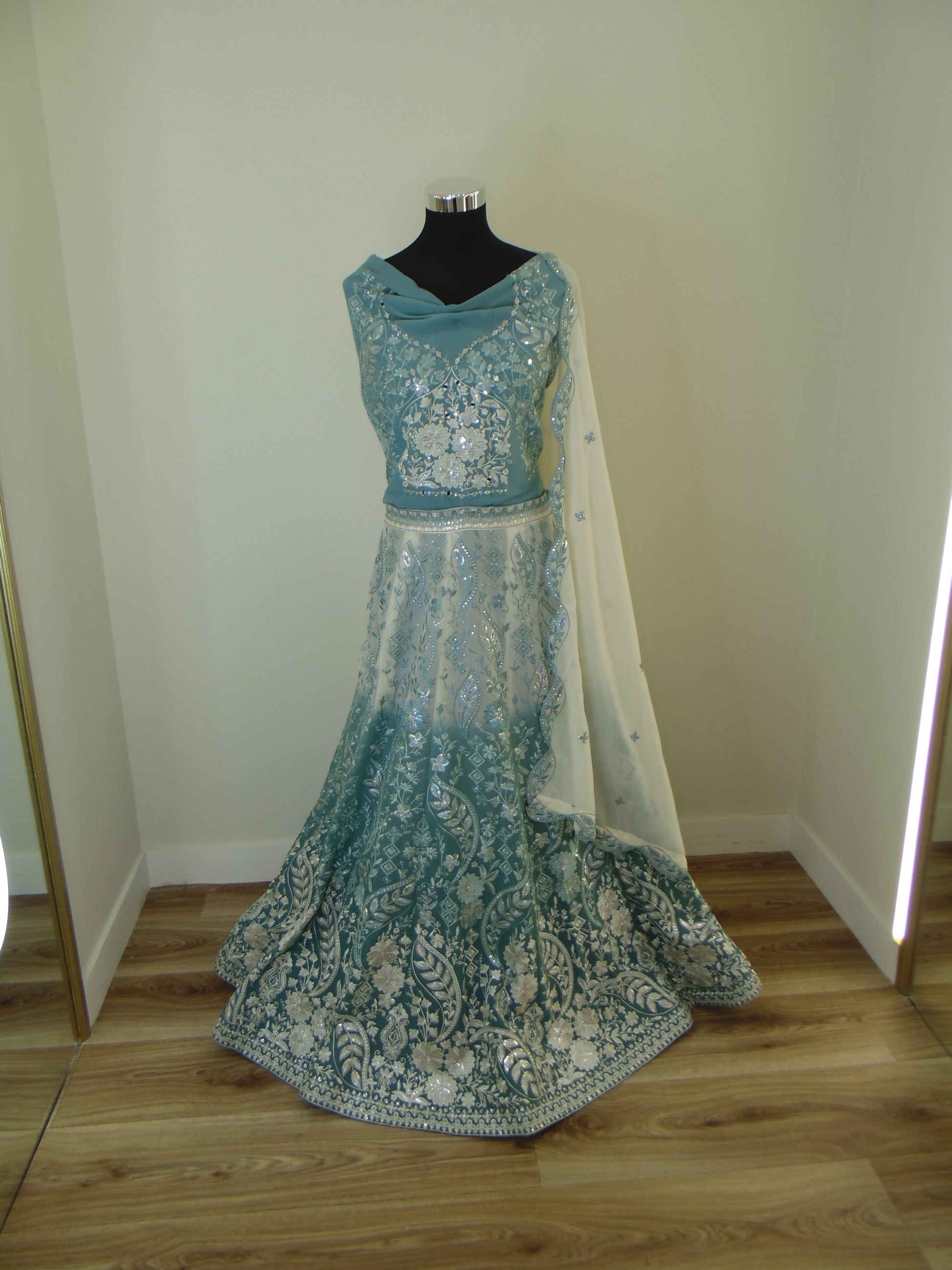 Teal embroidered Indian Lehenga on a mannequin against a white wall.