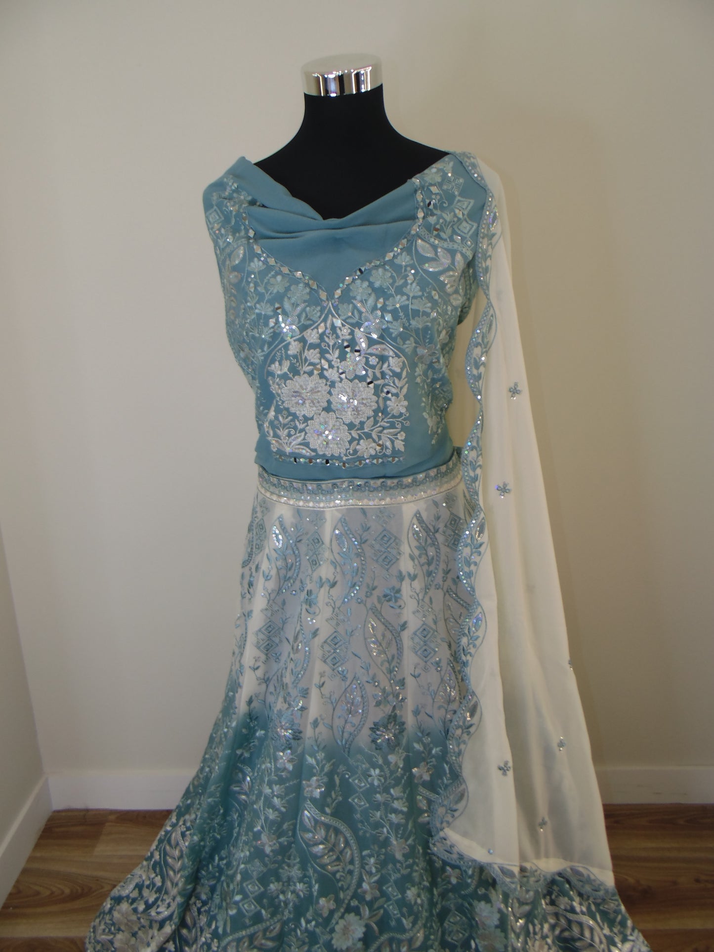 Teal and white embroidered Indian Lehenga on a mannequin against a plain wall.
