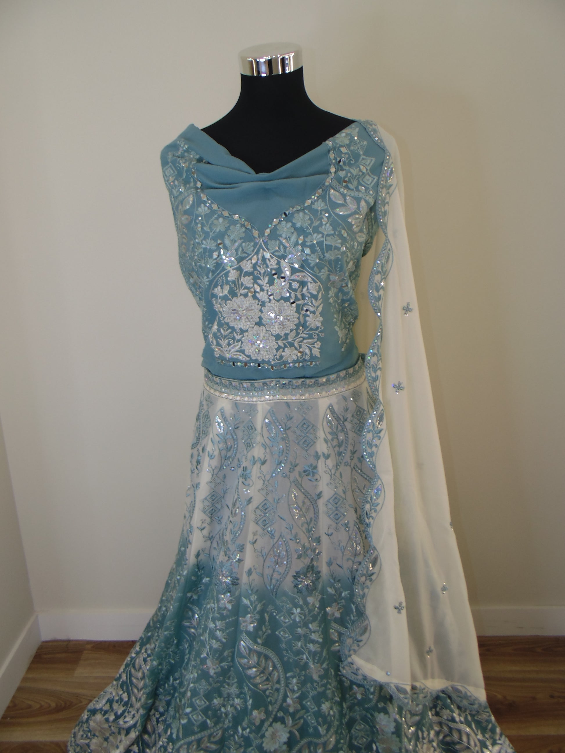 Teal and white embroidered Indian Lehenga on a mannequin against a plain wall.