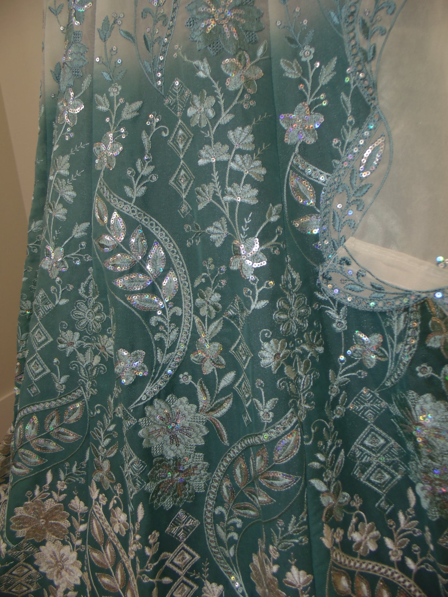 Close-up of green fabric with intricate silver embroidery and embellishments.