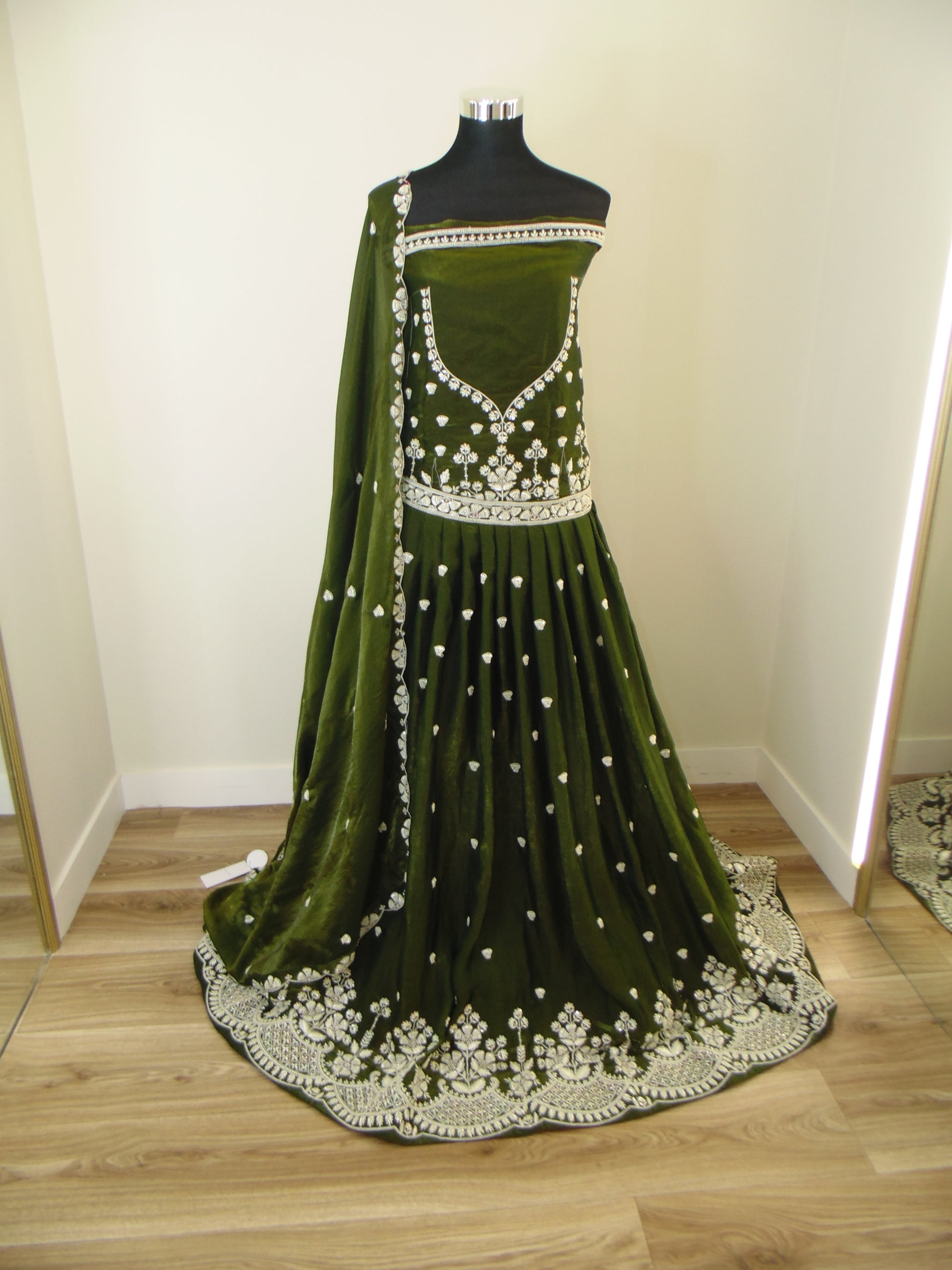 Green Indian Lehenga with white embroidery and pearl work on a wooden floor