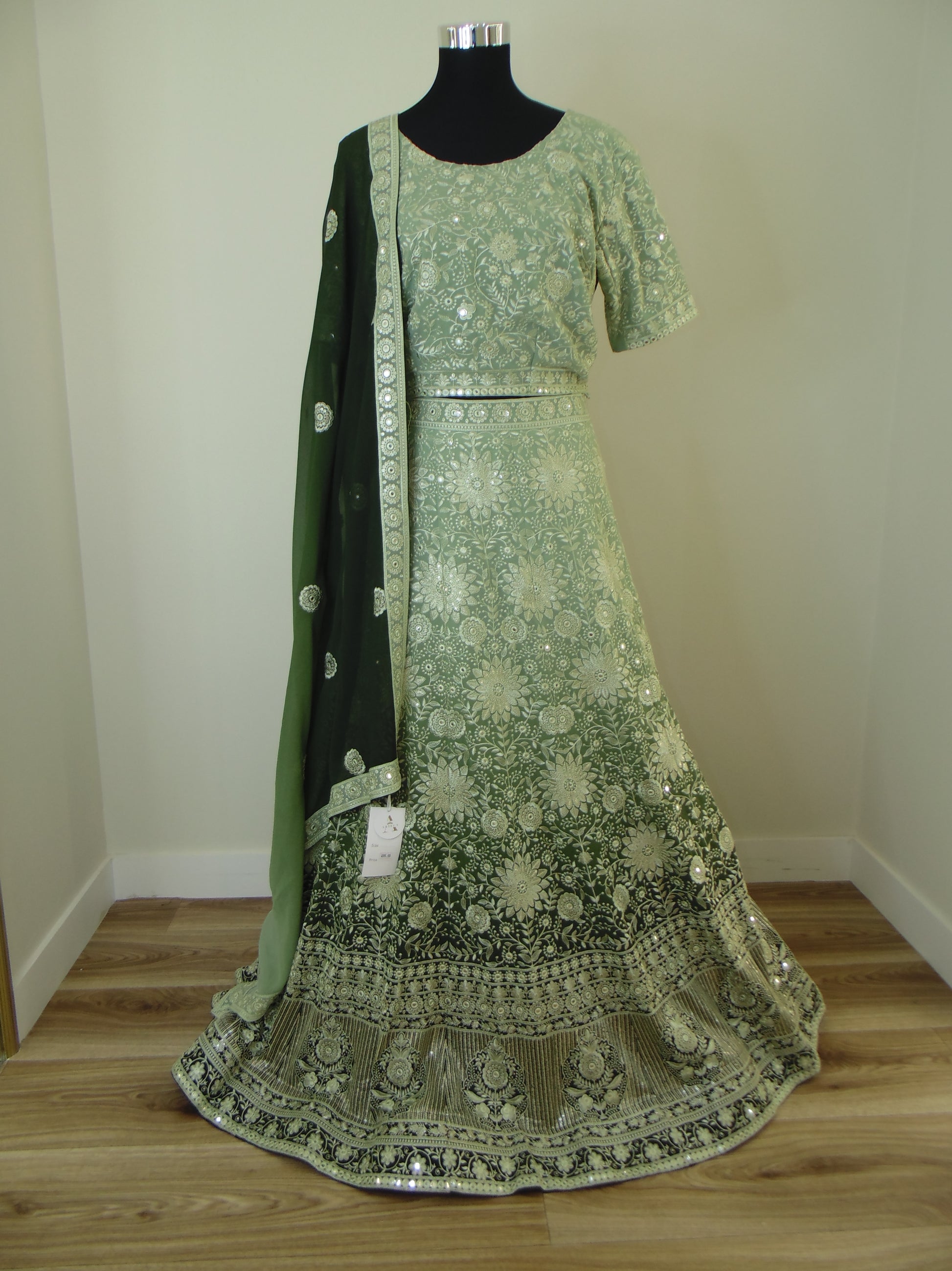 Green embroidered Indian Lehenga on a wooden stand against a white wall