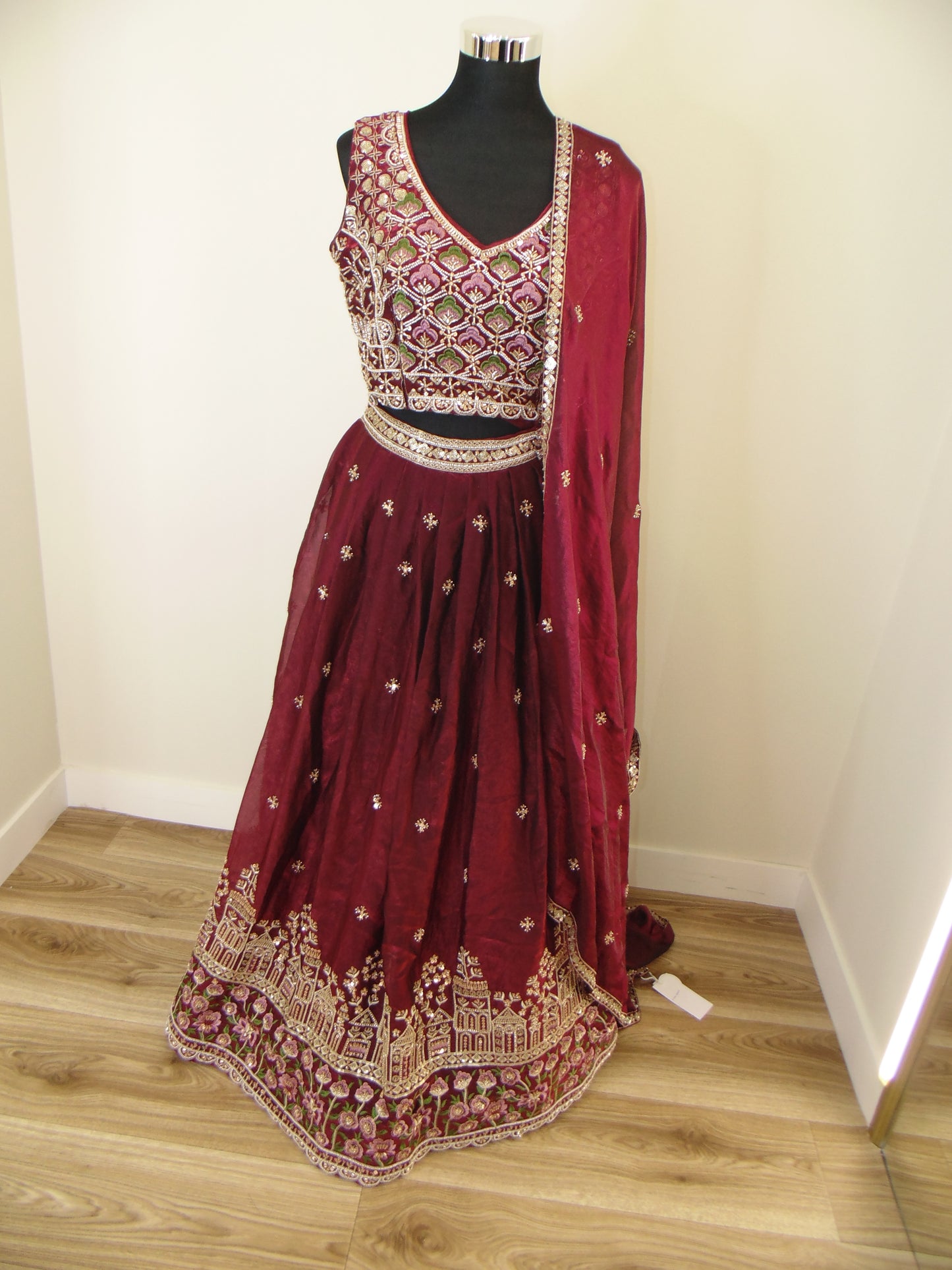 Maroon embroidered Indian Lehenga on a mannequin against a wooden floor background
