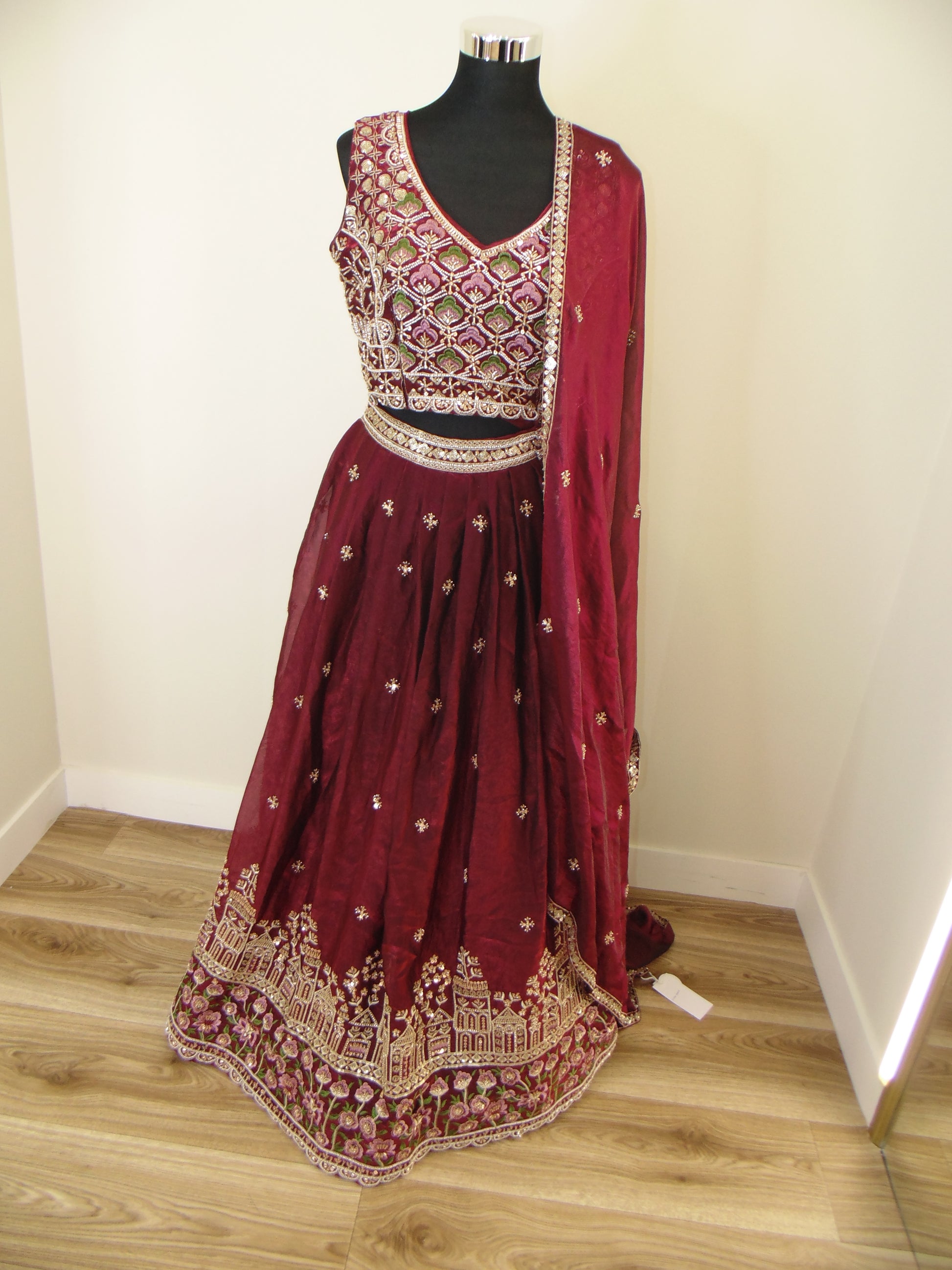 Maroon embroidered Indian Lehenga on a mannequin against a wooden floor background