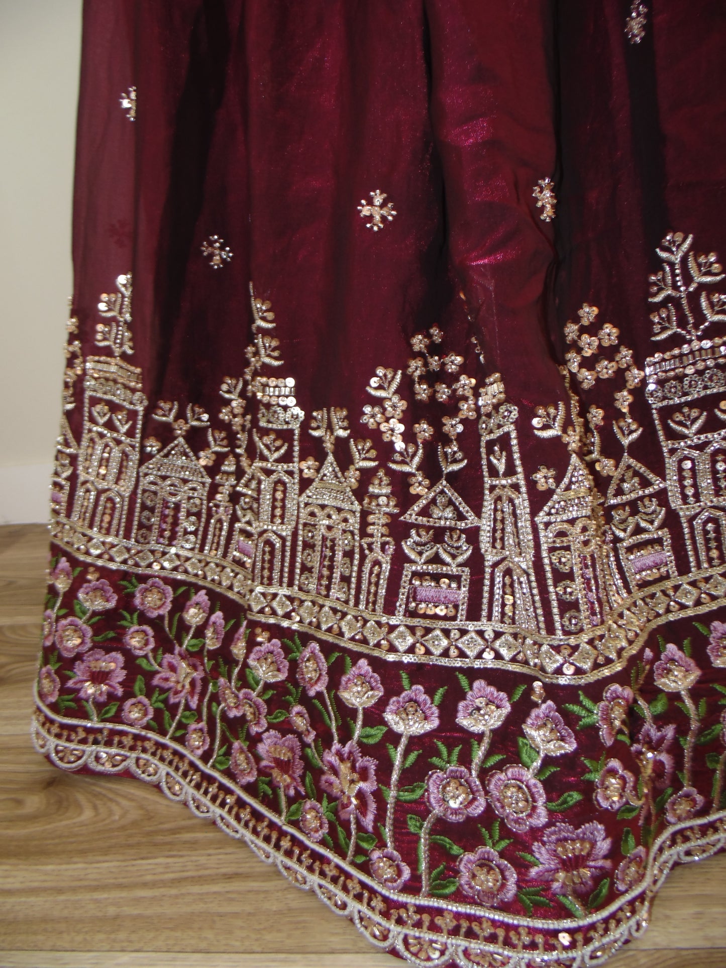 Maroon saree with gold and pink floral embroidery on a wooden surface