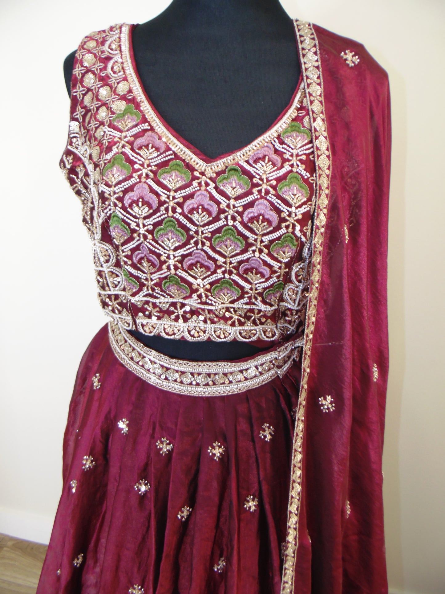 Maroon saree with intricate gold and green patterns on a white background