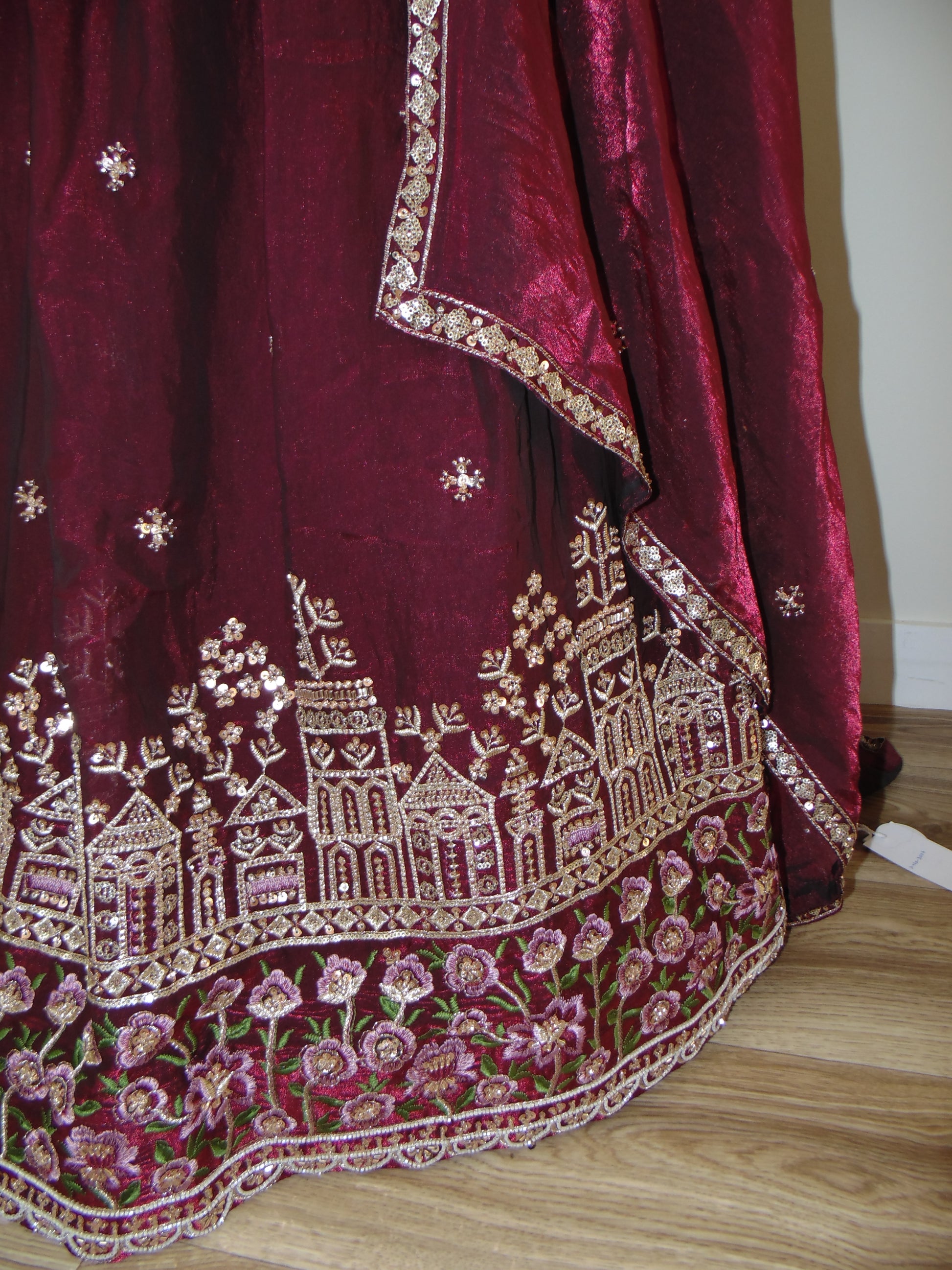 Maroon fabric with intricate gold and pink embroidery on a wooden surface
