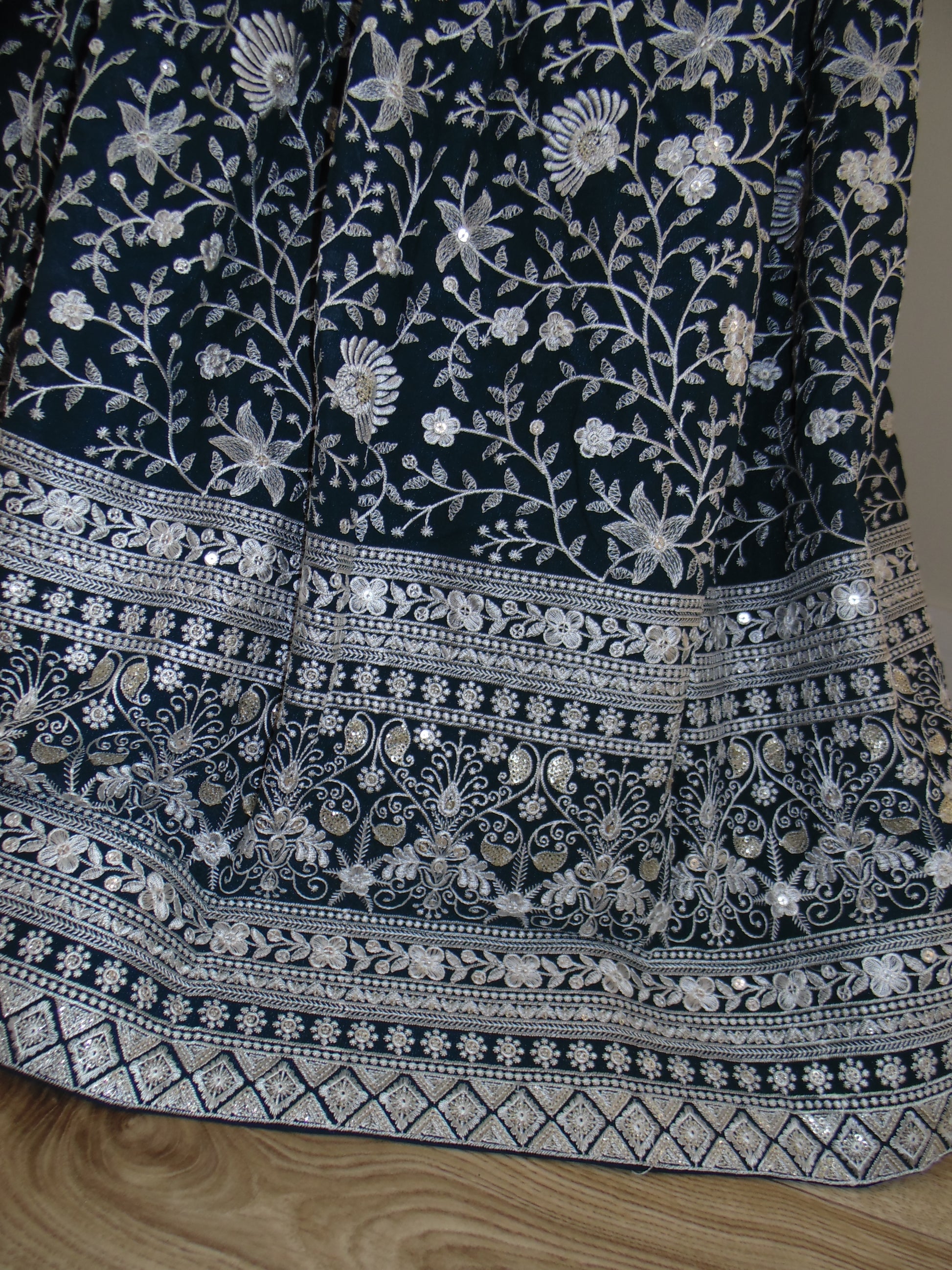 Dark blue fabric with intricate white floral embroidery on a wooden surface