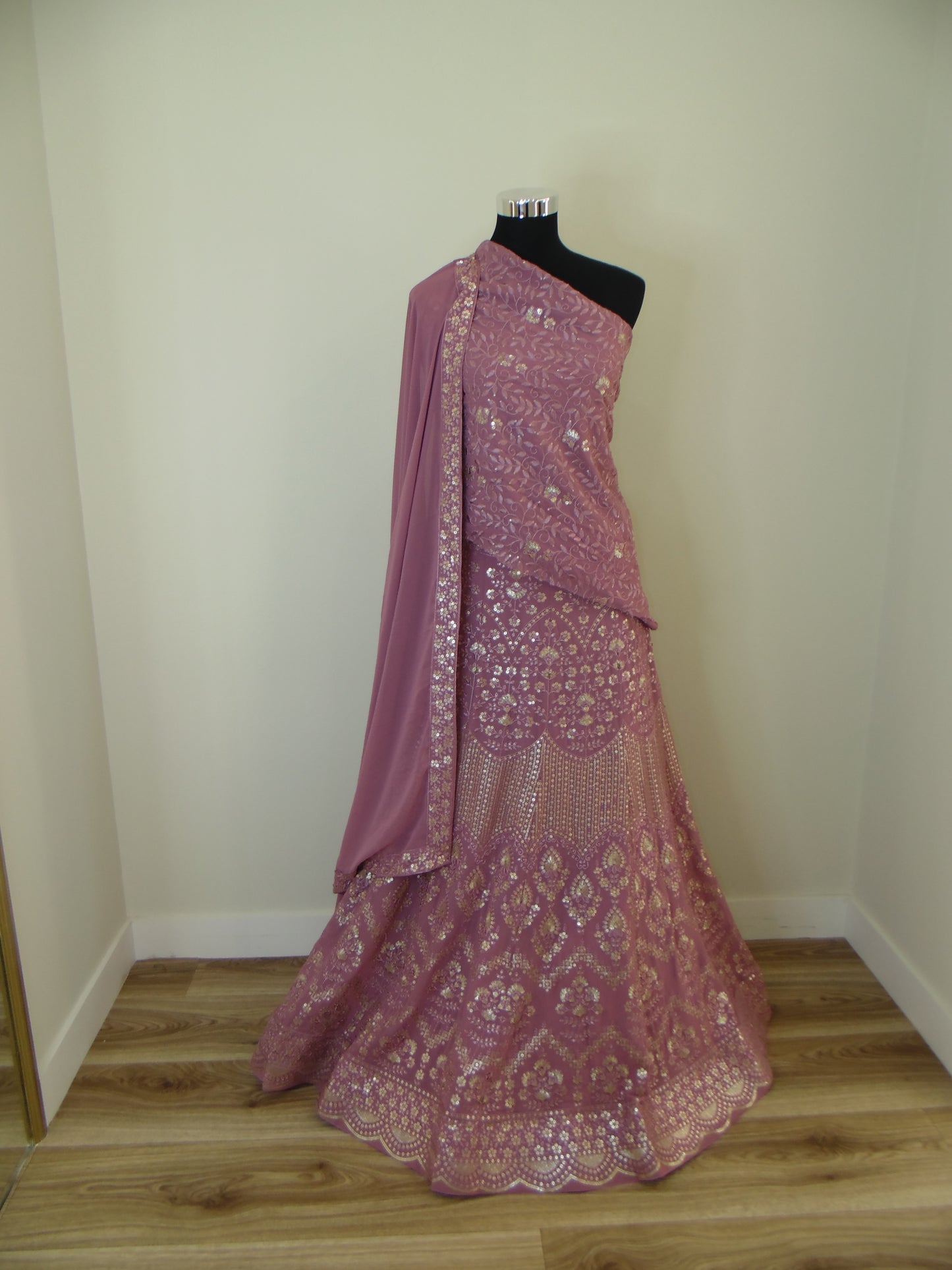 Pink lace Indian Lehenga on a mannequin against a plain wall.