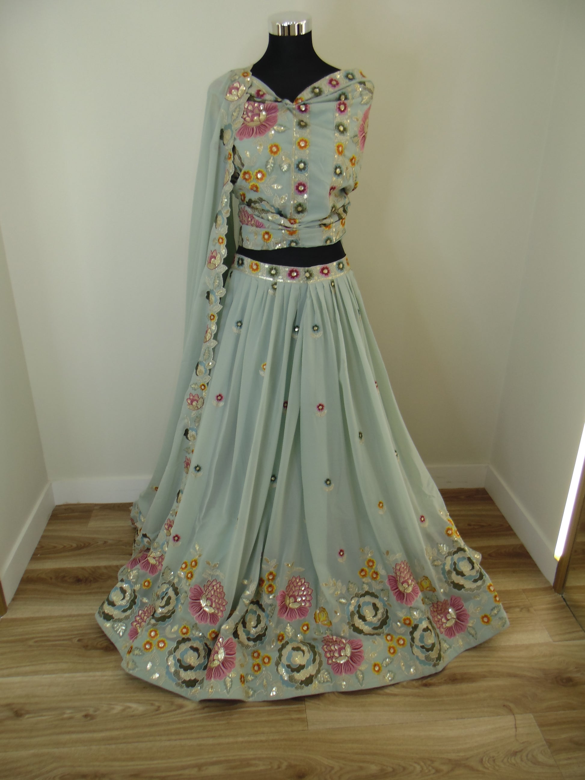 Light blue embroidered Lehenga on a wooden stand against a white wall.
