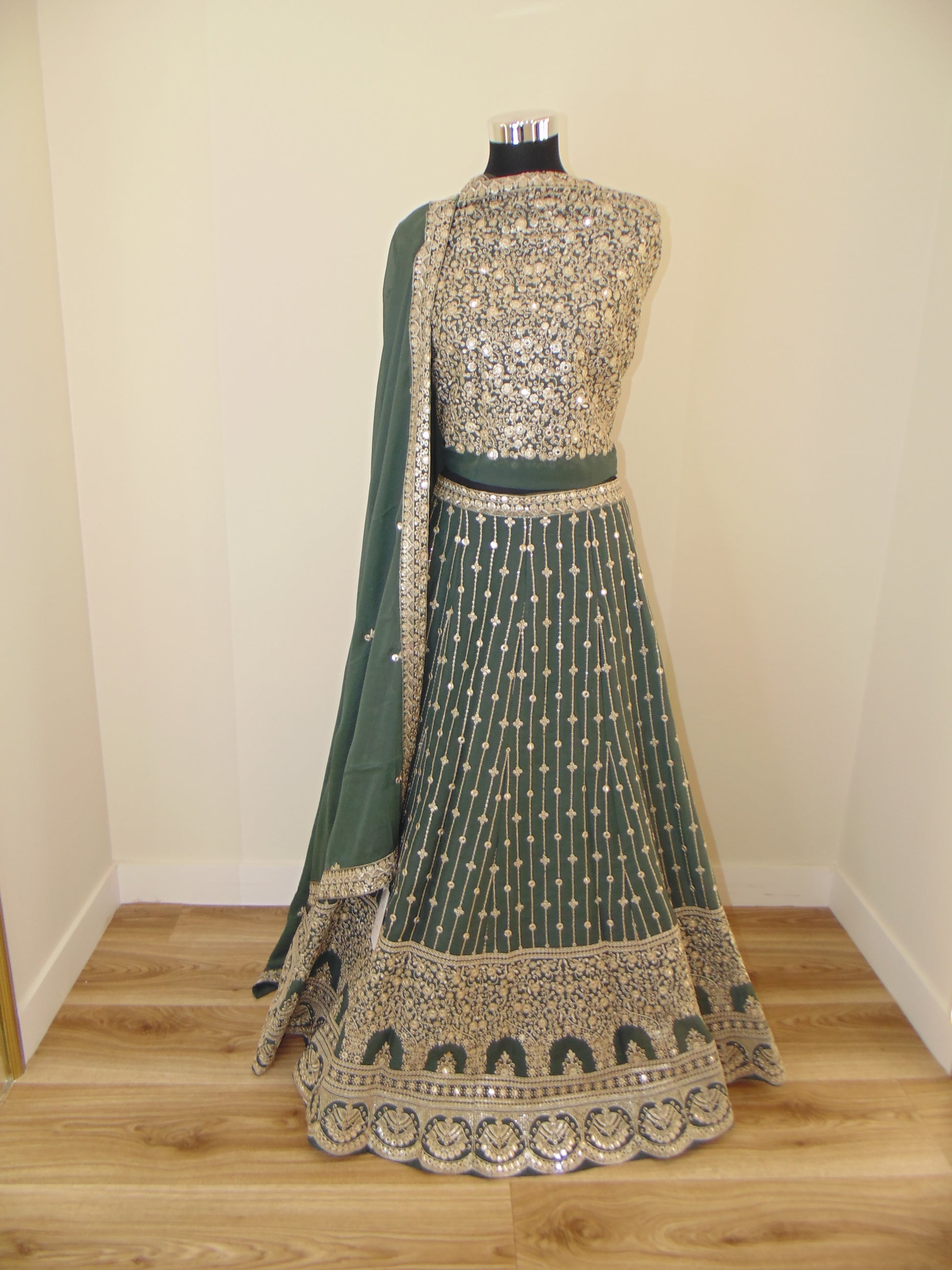 Green Indian Lehenga with silver border on a wooden hanger against a white wall