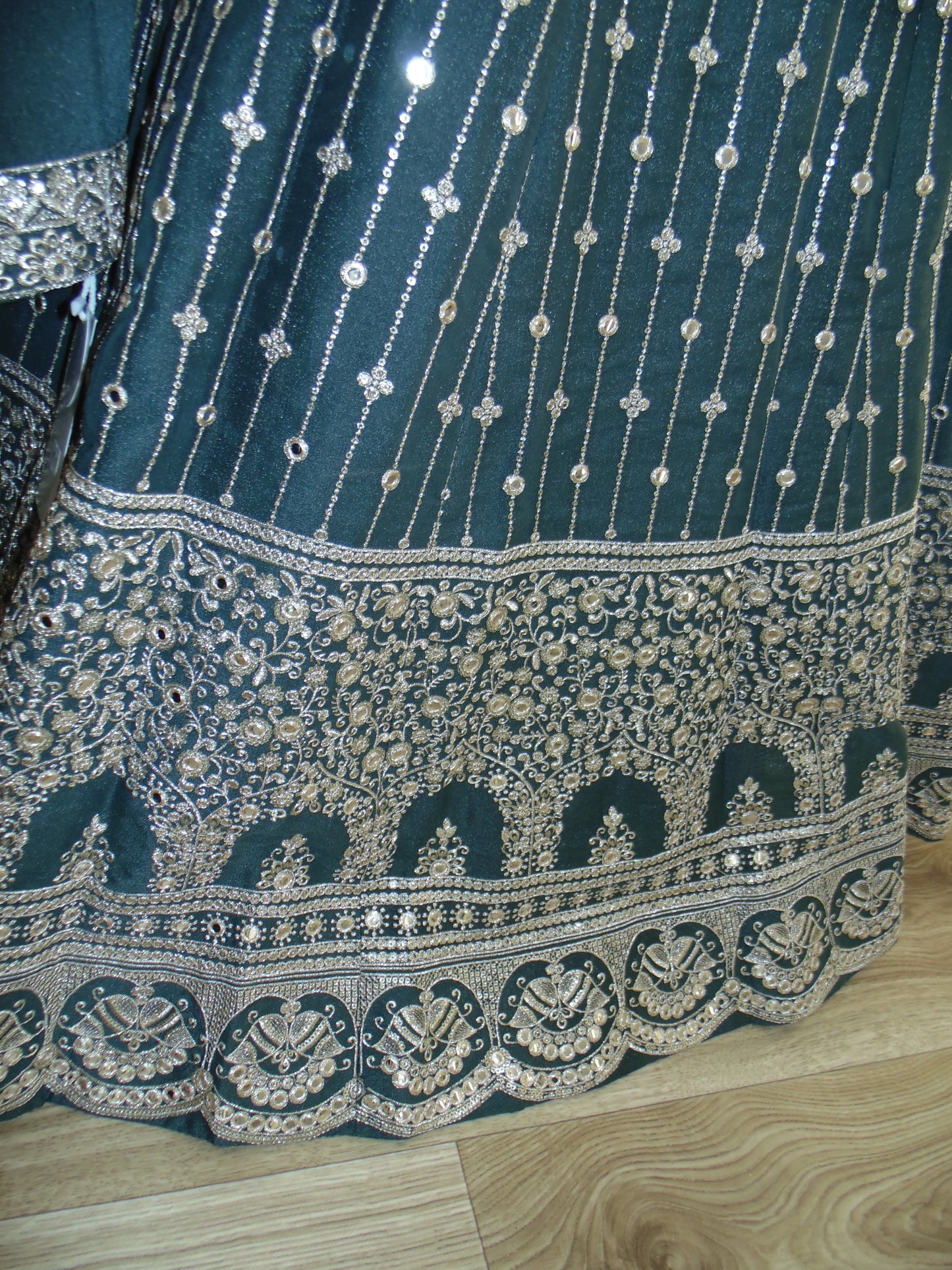 Close-up of a teal fabric with intricate silver embroidery on a wooden floor.