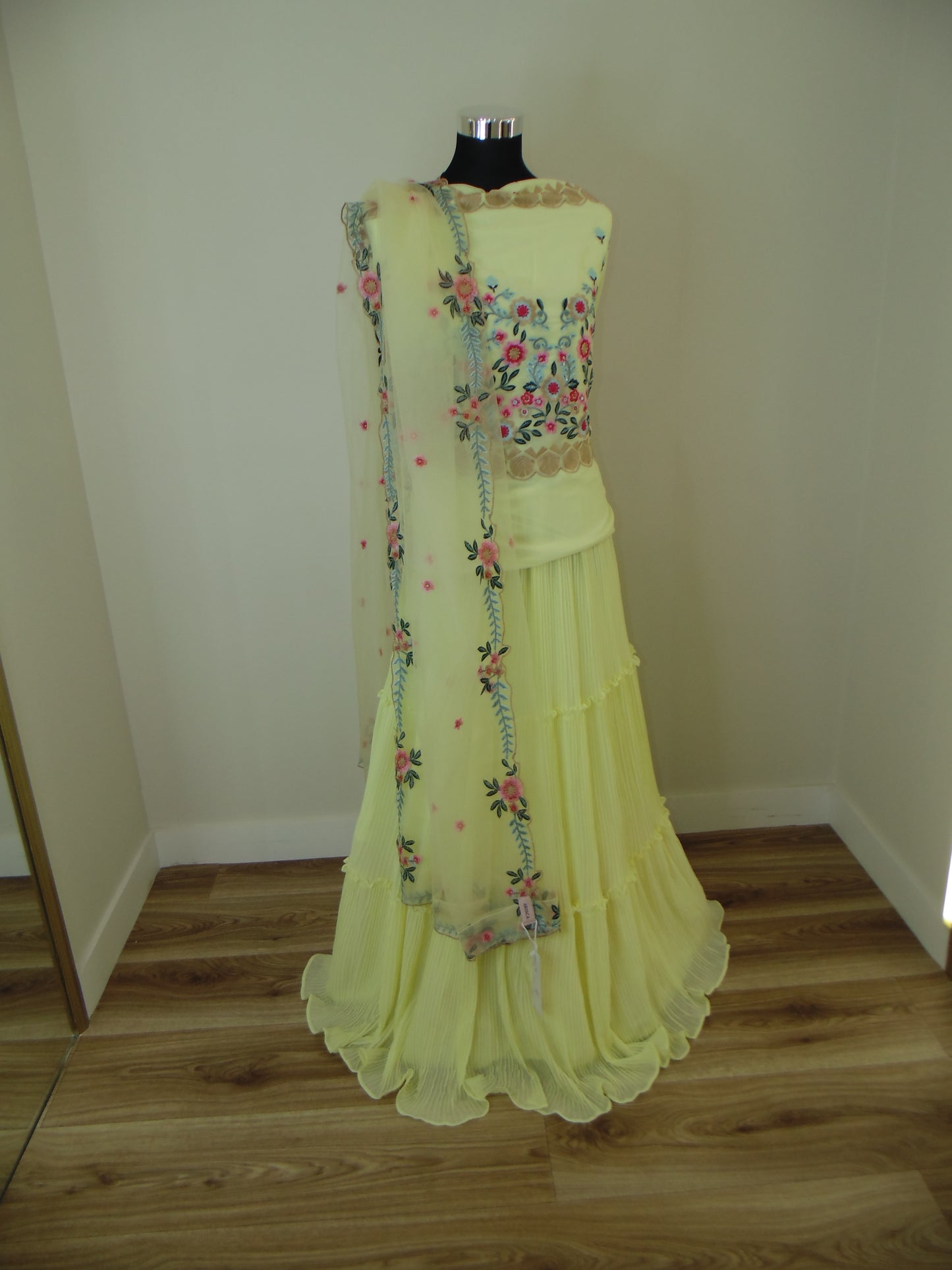Yellow Skirt with floral embroidery on a mannequin against a wooden and white background