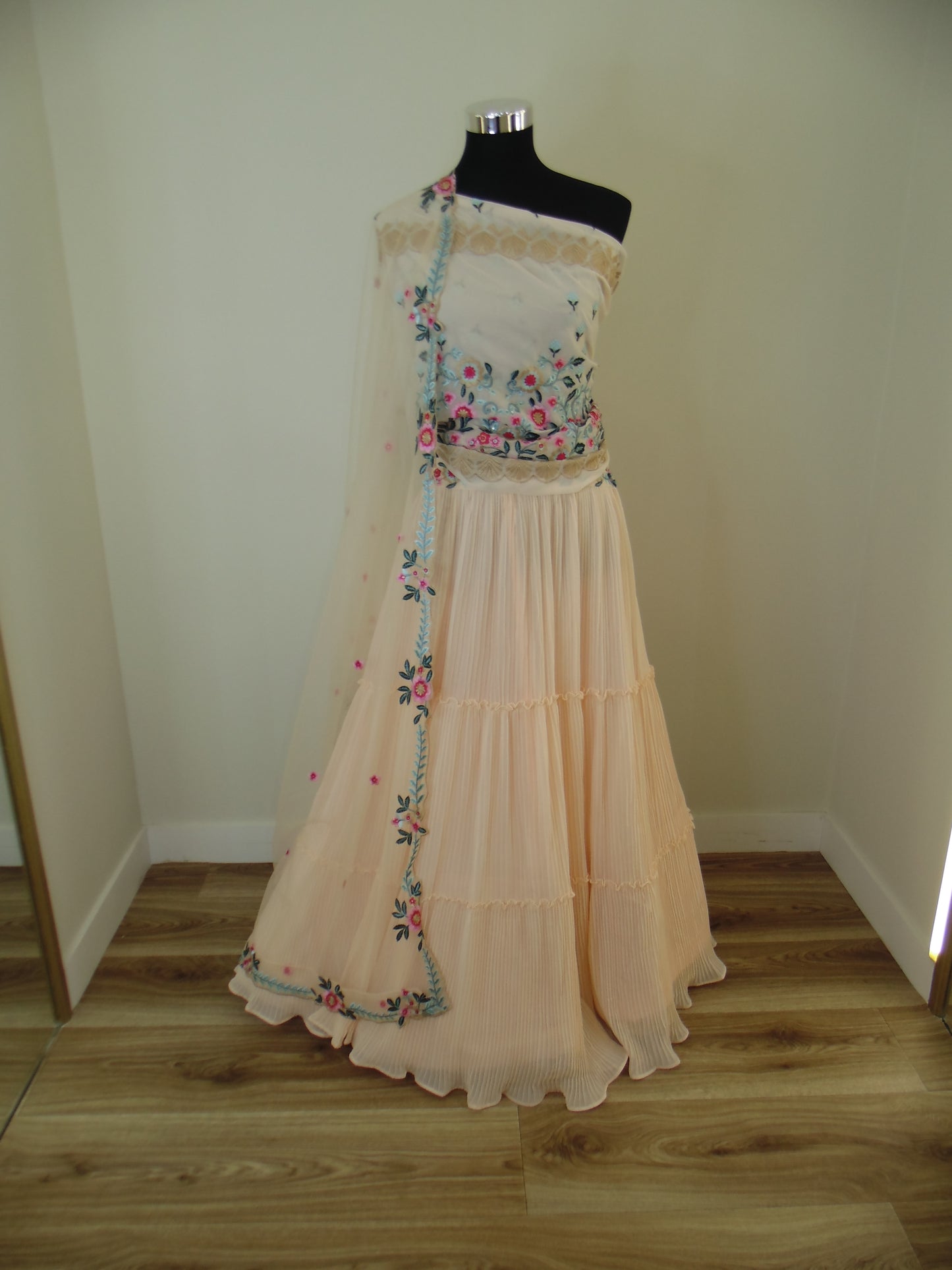 Mannequin wearing a peach-colored dress with floral embroidery on a shelf.