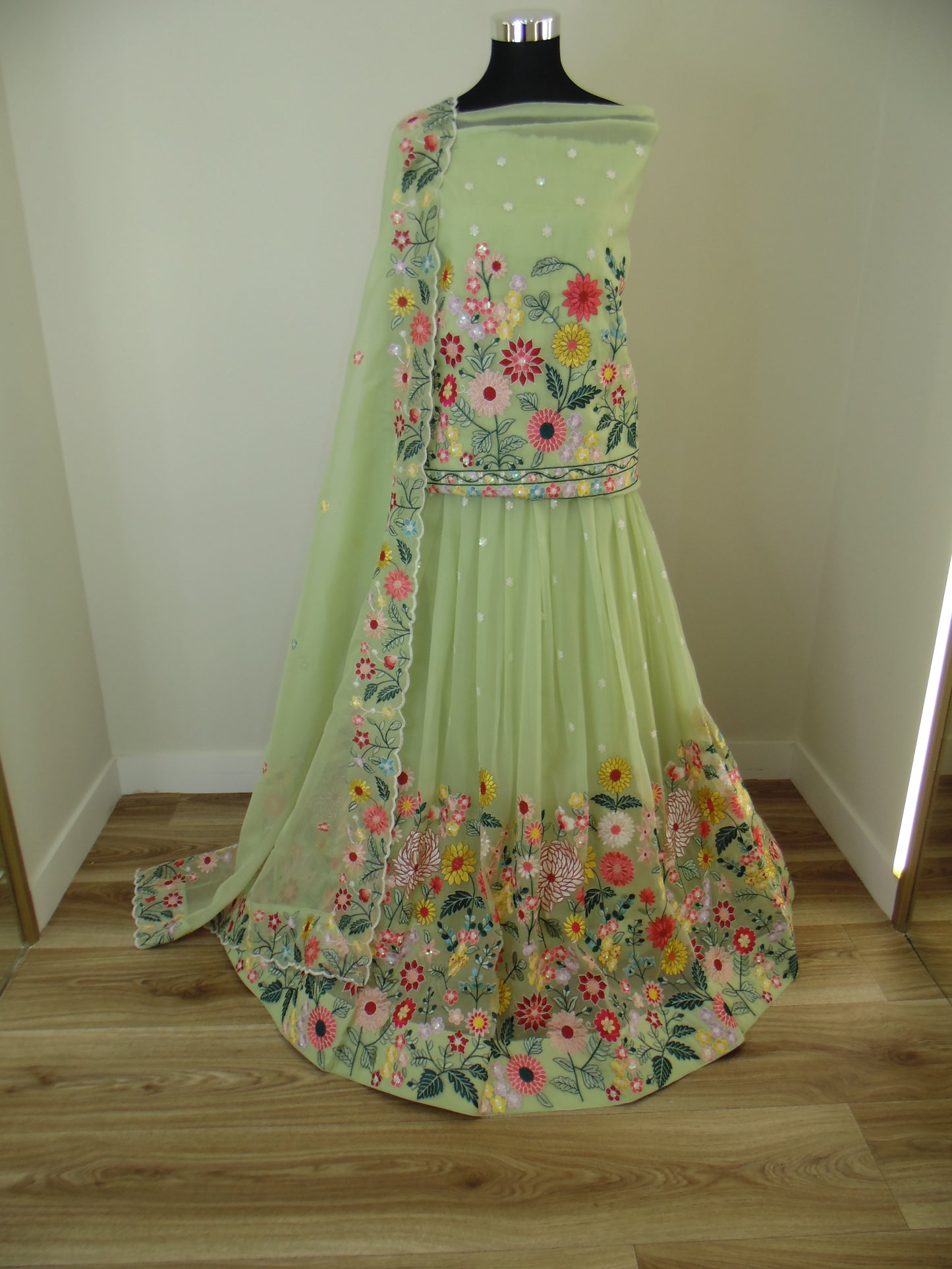 Green Indian Lehenga with floral patterns on a mannequin against a wooden wall.
