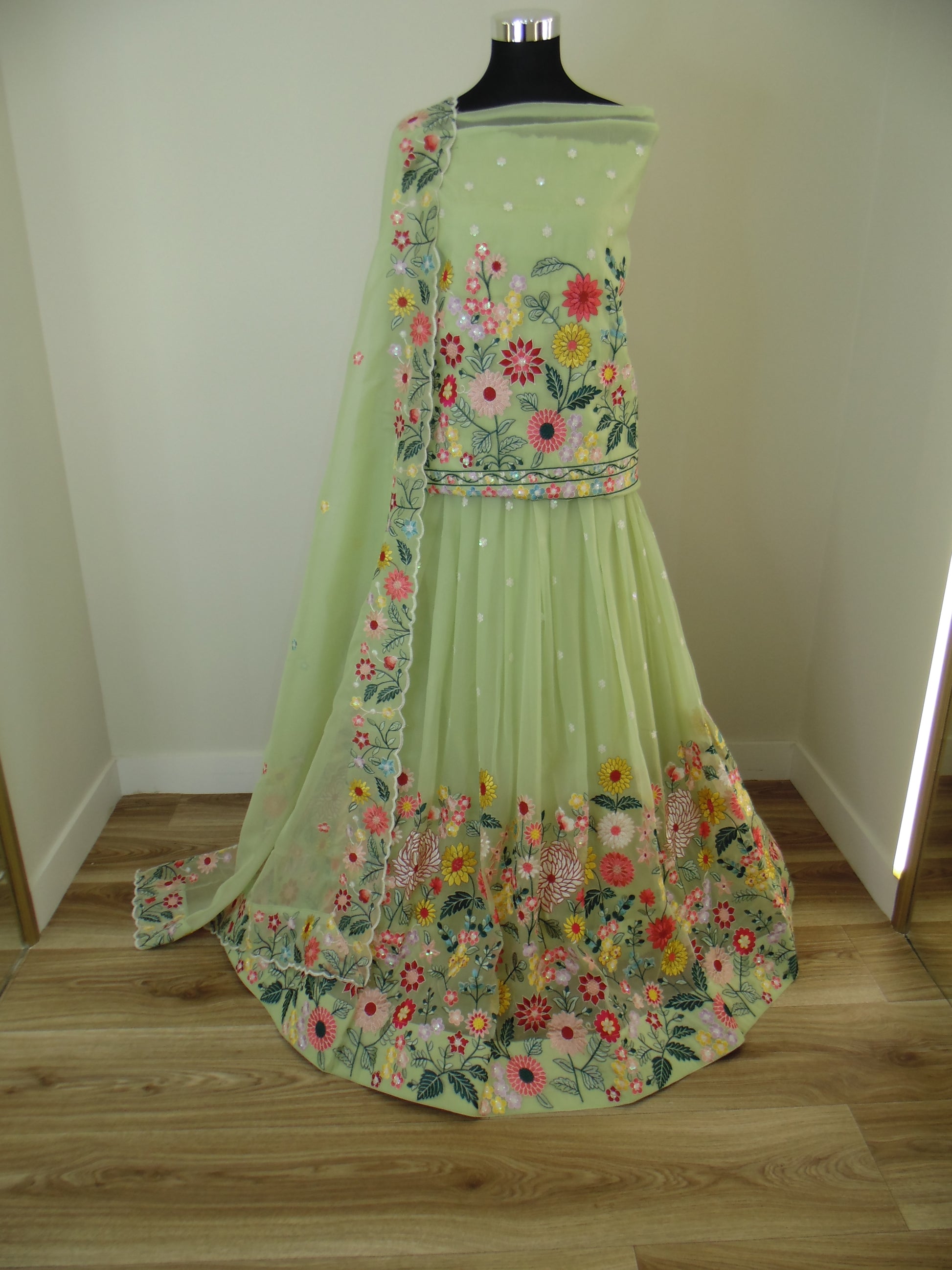 Green Indian Lehenga with floral patterns on a mannequin against a wooden wall.