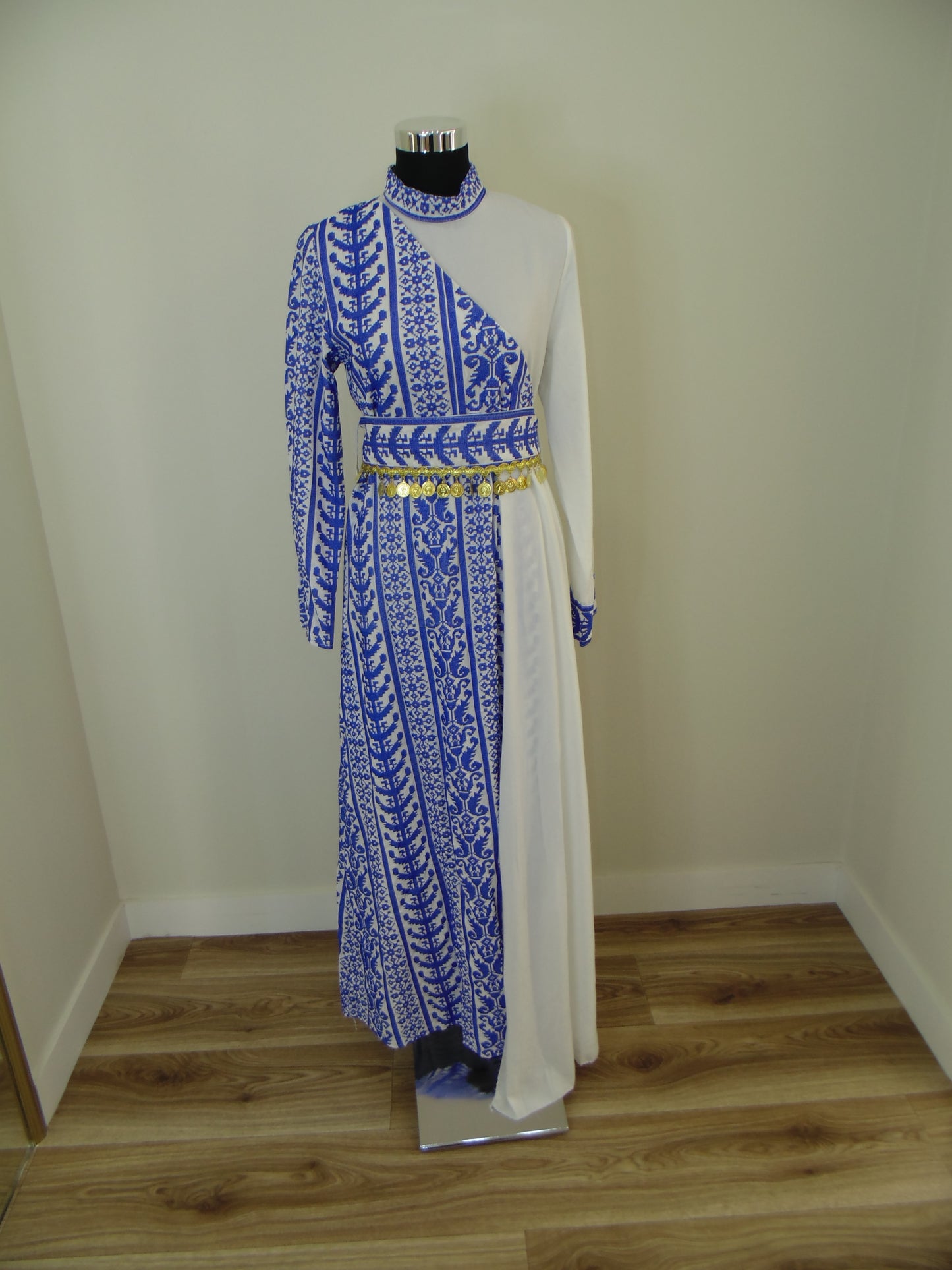Traditional embroidered Palestinian Thobe on a white shelf against a wooden wall.