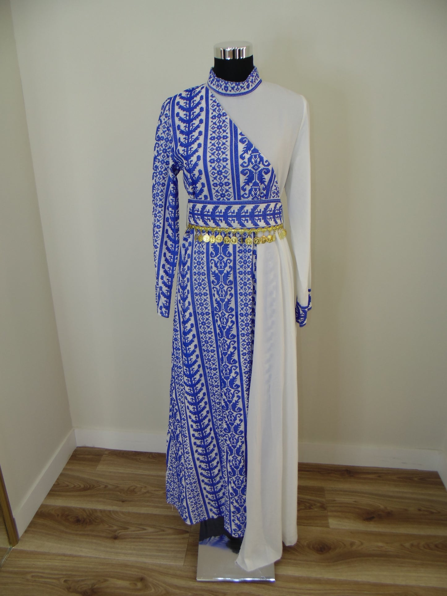 Traditional embroidered garment on a white stand against a plain wall.