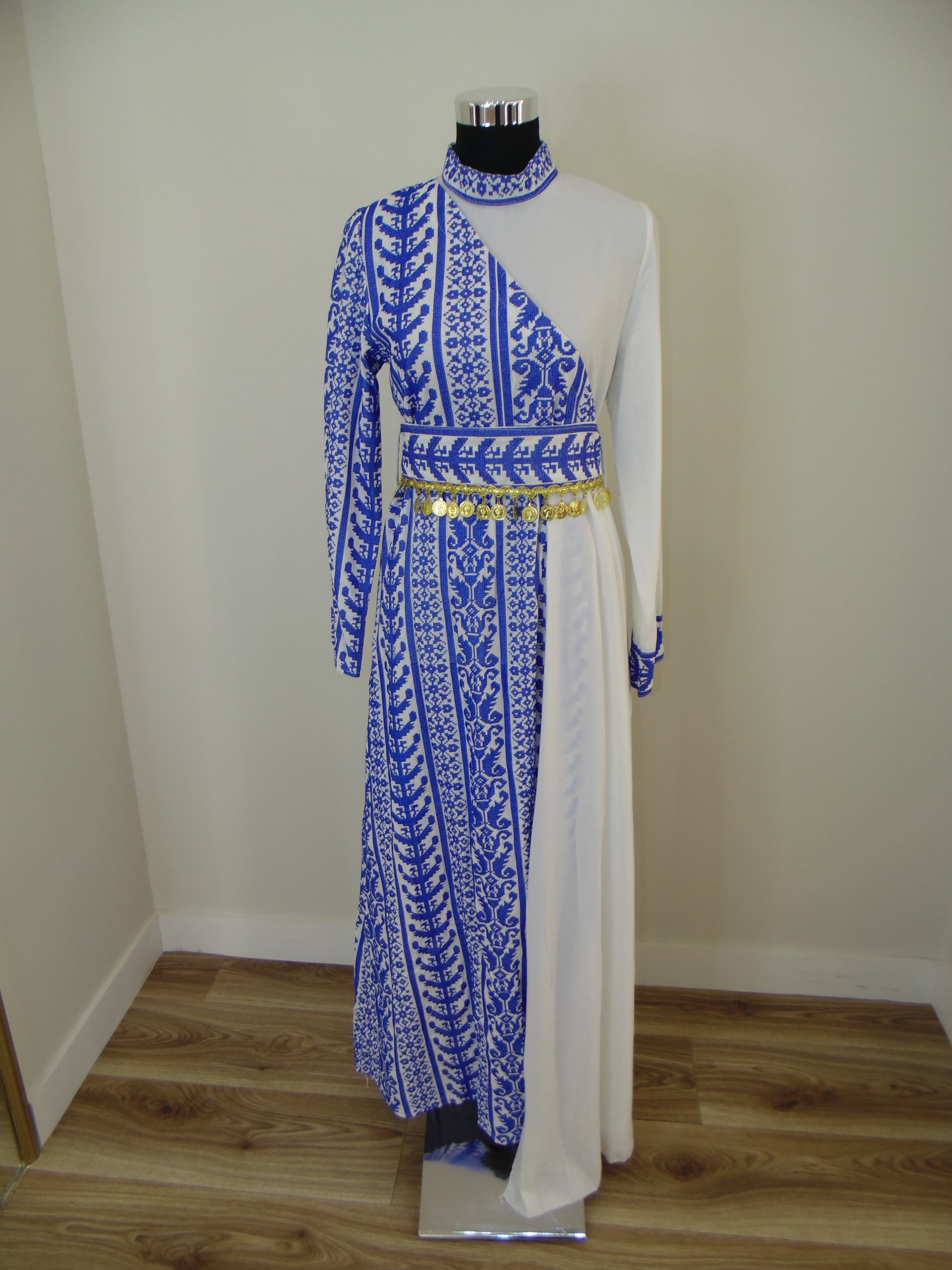 Traditional embroidered garment on a white stand against a plain wall.